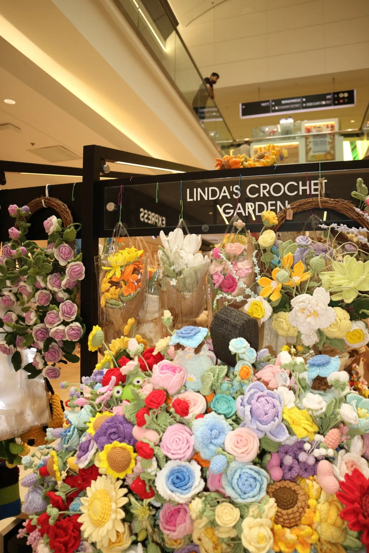 Display of colorful, handmade crocheted flowers at Linda's Crochet Garden in a shopping mall.