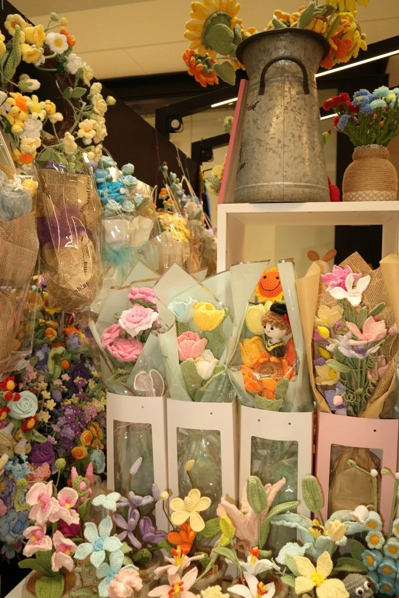 Display of colorful handmade felt flower bouquets and plush toys in a store.
