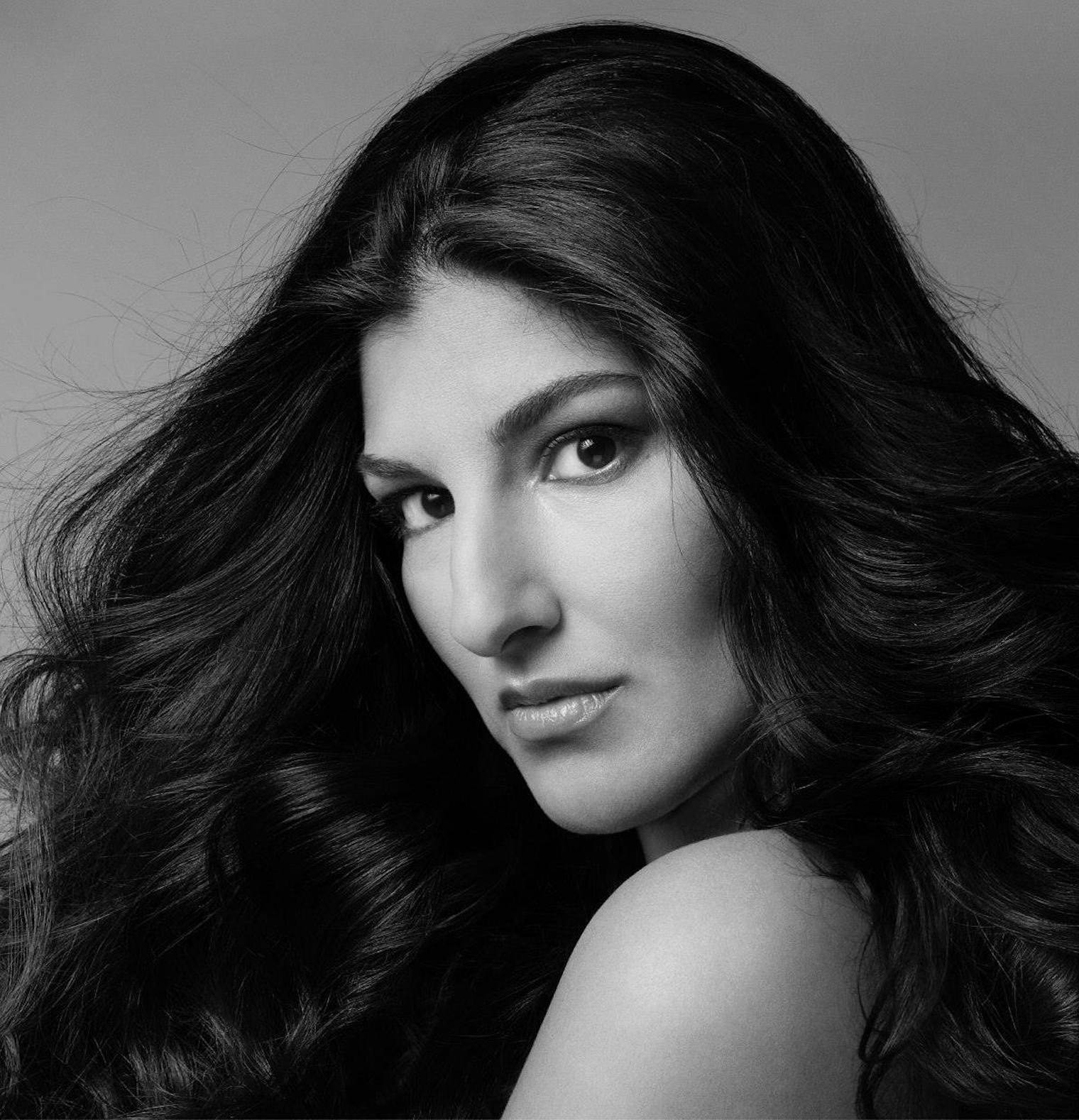 Black and white portrait of a woman with long, wavy hair, looking directly at the camera with a serious expression.