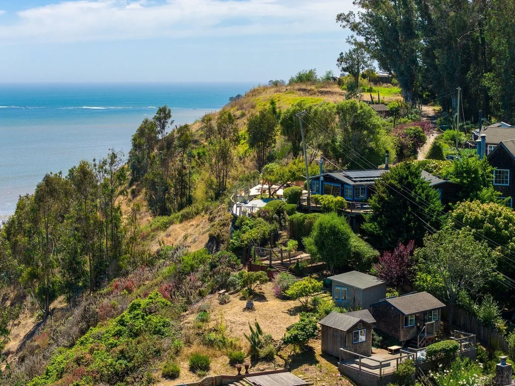 Hilly coastal landscape with houses, trees, and ocean view in the background.