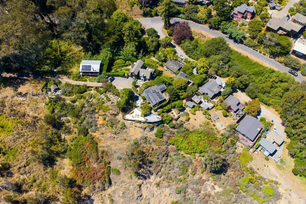 Aerial view of a residential neighborhood on a hillside with houses, trees, and a winding road.