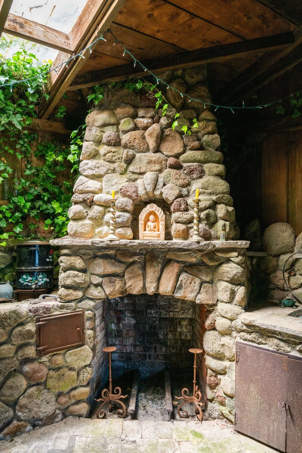 Stone fireplace with a small Buddha shrine and two candles on top, surrounded by greenery and rustic decor.