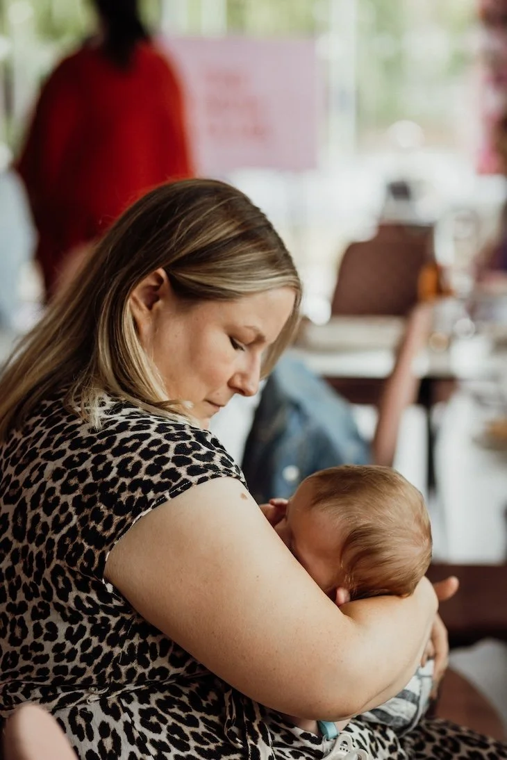 A woman with blonde hair wearing a leopard print shirt is holding and comforting a young child in her arms in an indoor setting with blurred background.