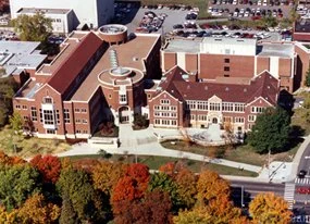 Aerial view of a large brick school building surrounded by trees with colorful fall foliage and parking lots.