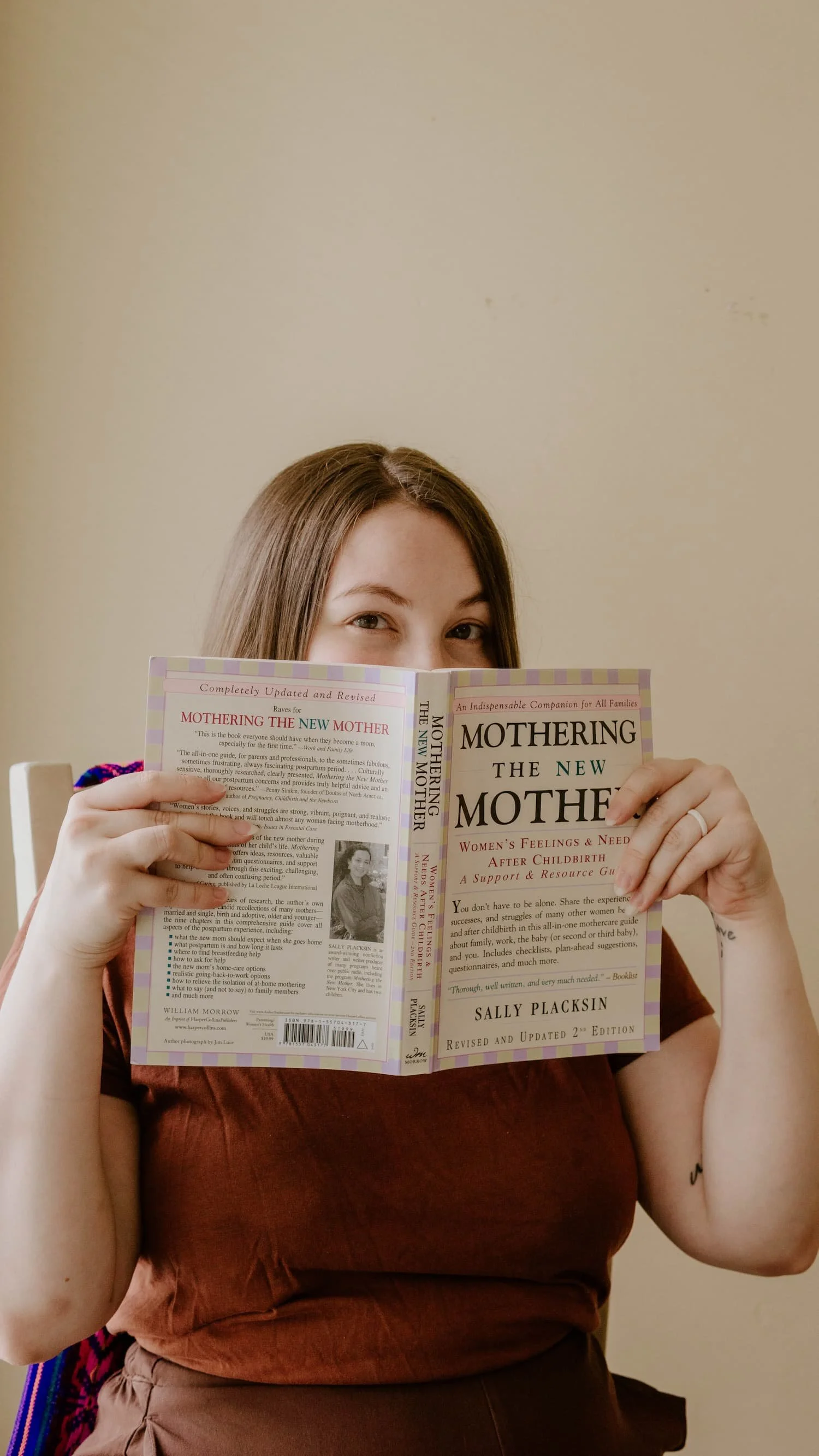Birth & Postpartum Doula, Hannah Servis, peering over the top of a book reading about how to mother the mother in the postpartum period after birth.