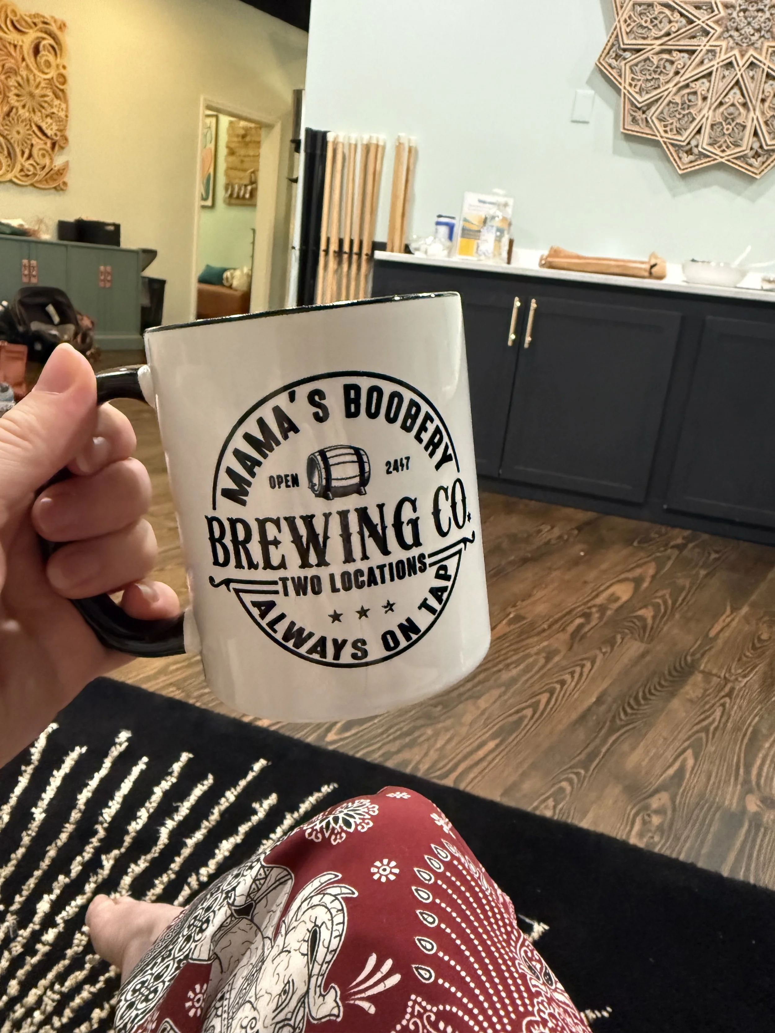 Doula, Hannah Servis, holding a coffee mug with the words "Mama's Boobery always on tap" on the front of the mug as she gets ready to provide breastfeeding support to her clients.