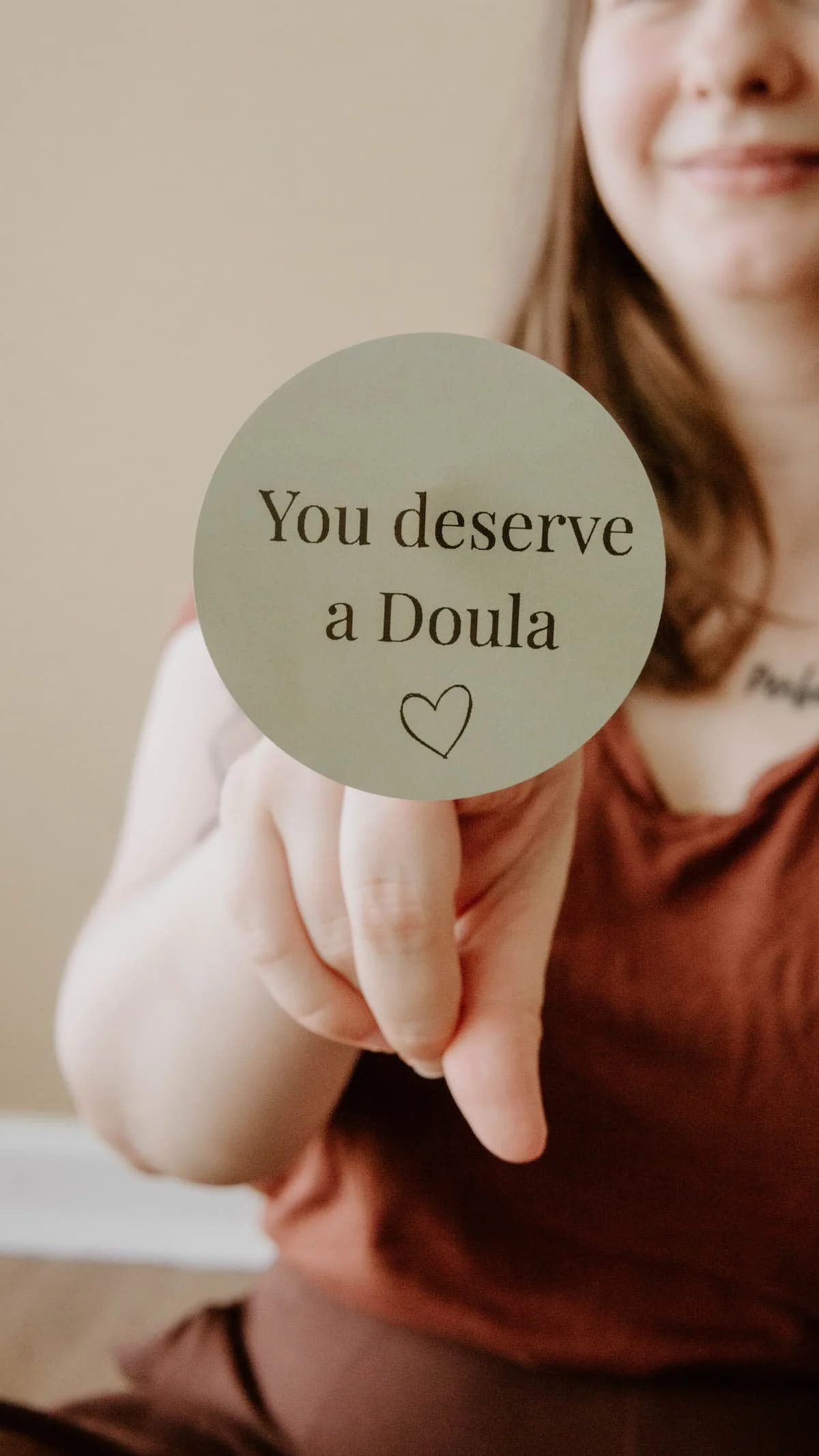 Birth and postpartum doula, Hannah Servis, holding a green circle sticker on her finger that says "You deserve a doula".