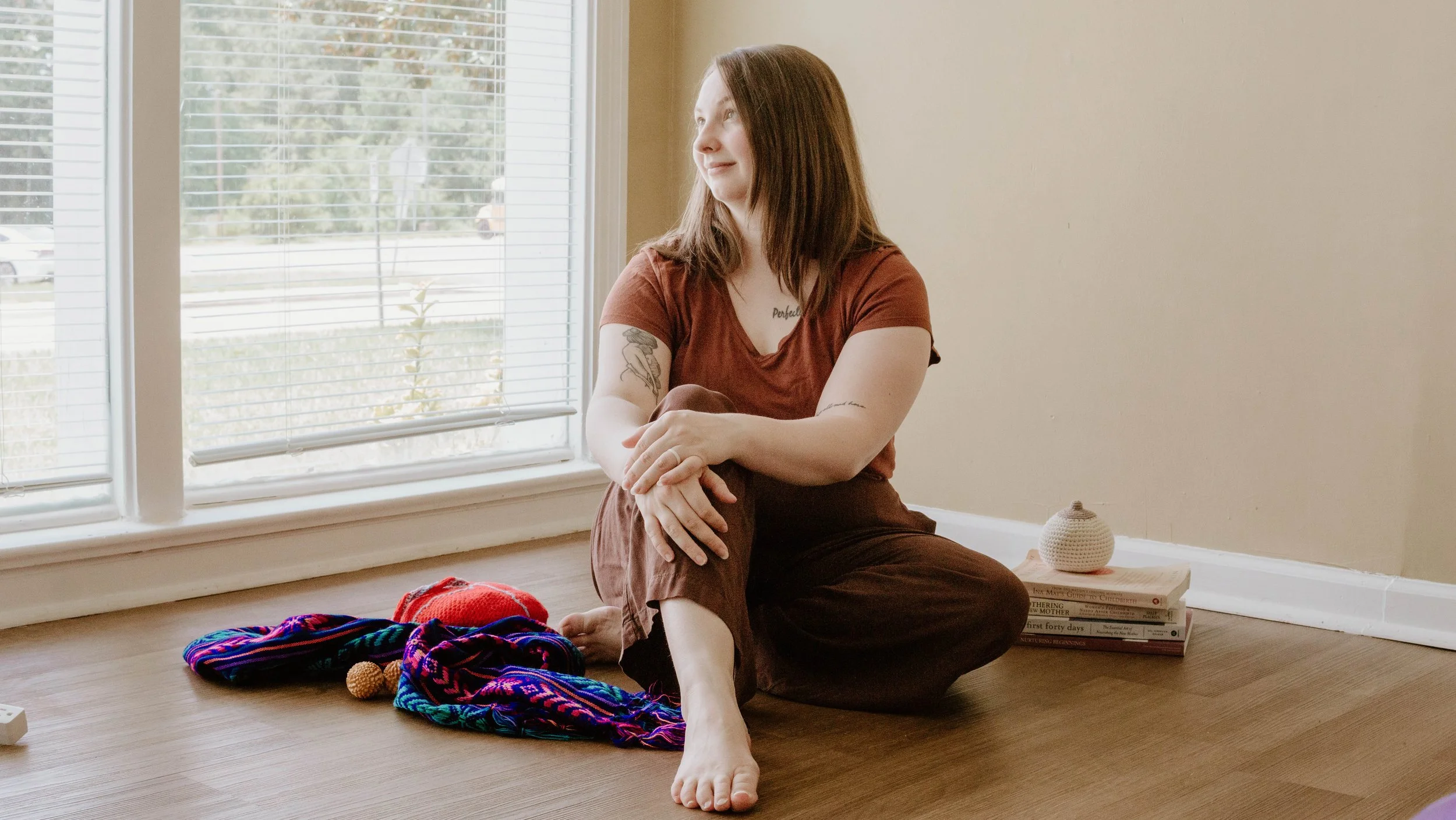 Birth doula, Hannah Servis, relaxing on the floor as she stares out the window daydreaming about supporting moms in labor and birth.