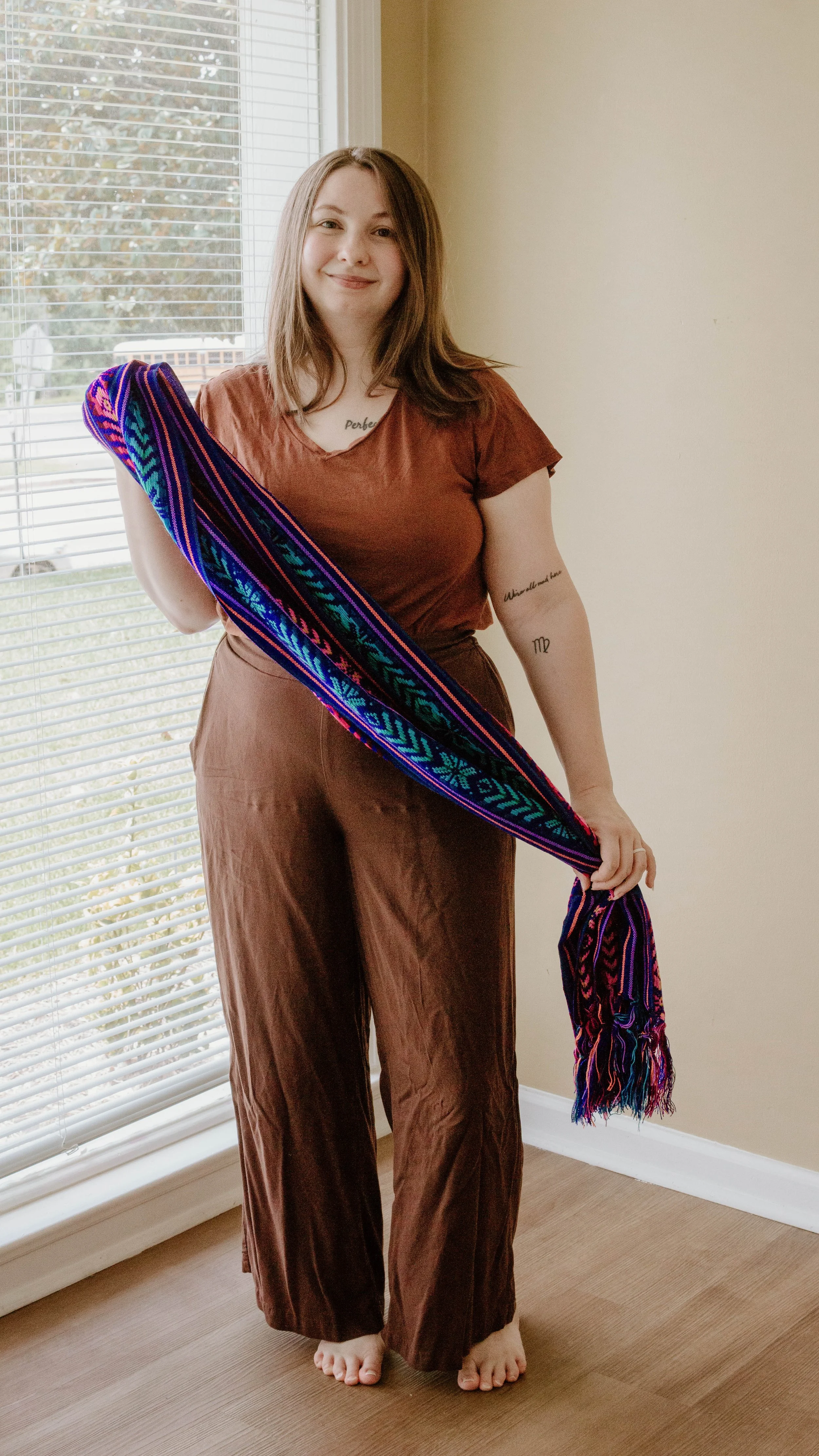 Birth Doula, Hannah Servis, standing infront of a window holding a rebozo across her body as she smiles, getting ready to support a mom in labor in Jackson, Mississippi.