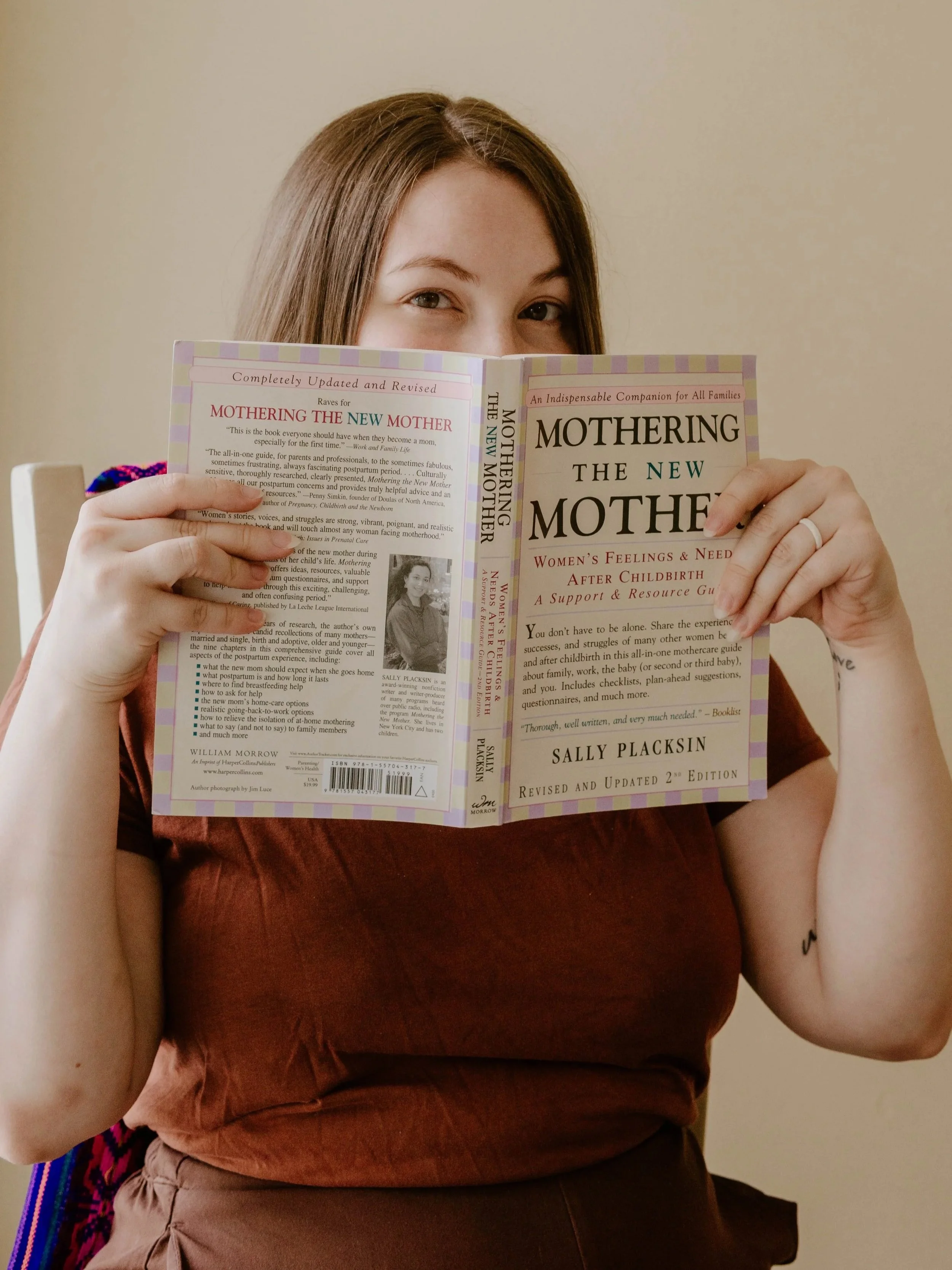 Birth & Postpartum Doula, Hannah Servis, peering over the top of a book reading about how to mother the mother in the postpartum period after birth.