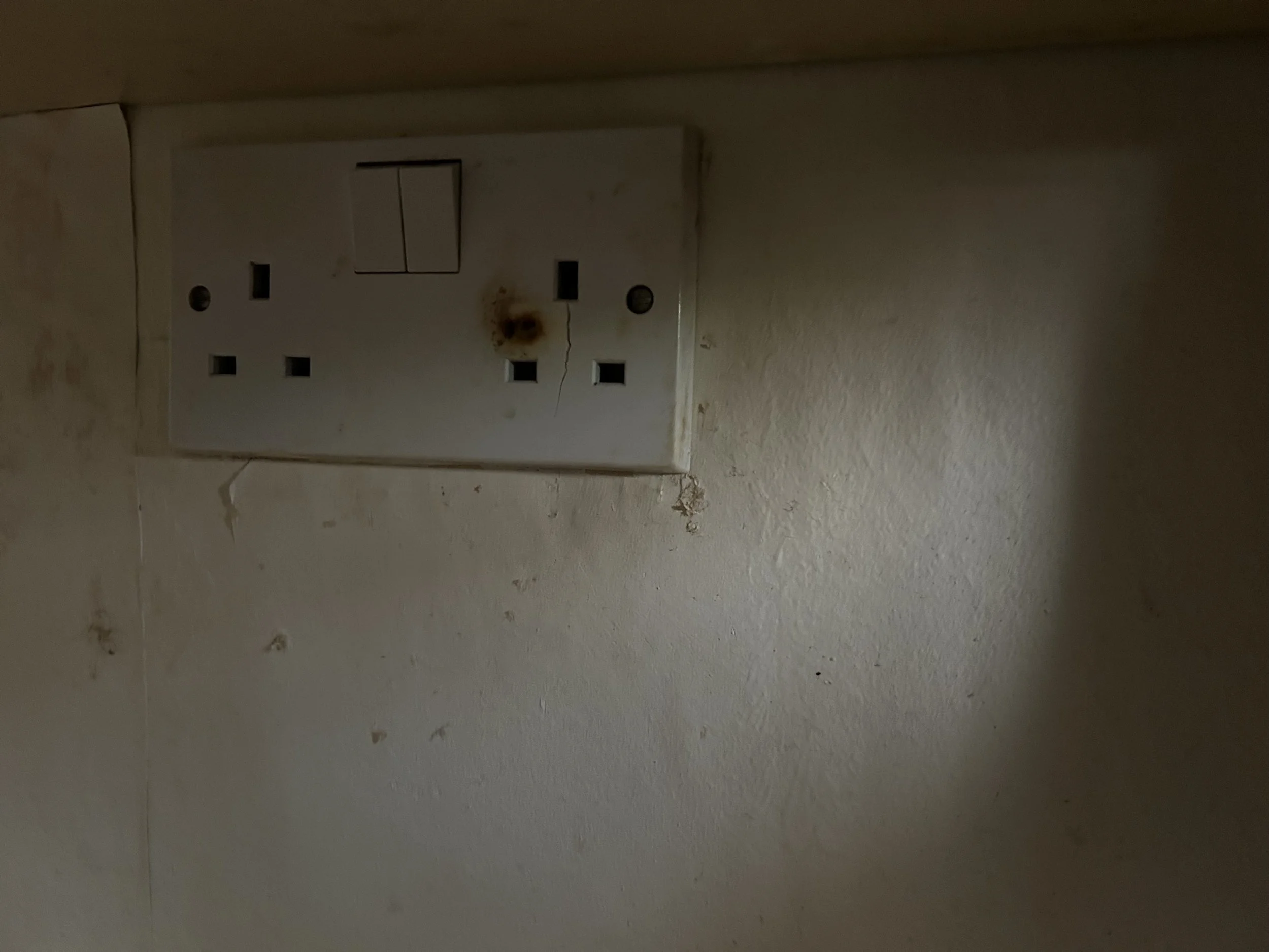 An electrical wall socket with two ports and a switch, stained with rust and embedded in a dirty, stained wall.