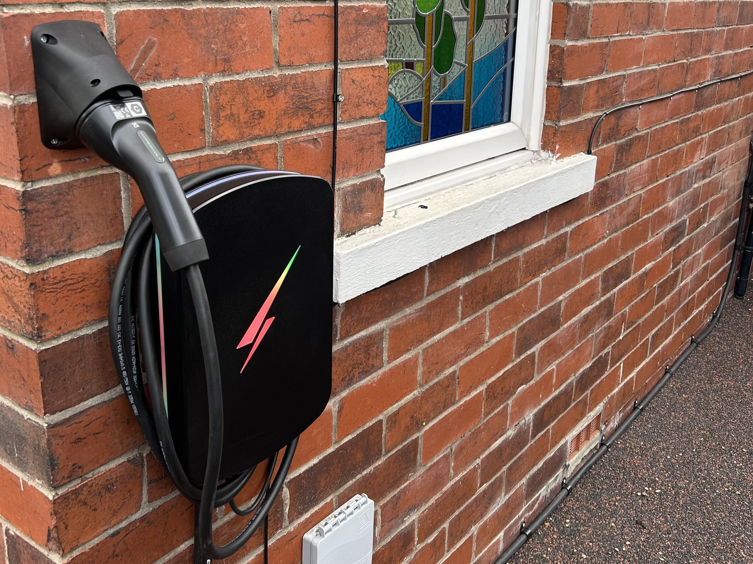 Electric vehicle charging station mounted on a red brick wall with black charging cable coiled nearby.