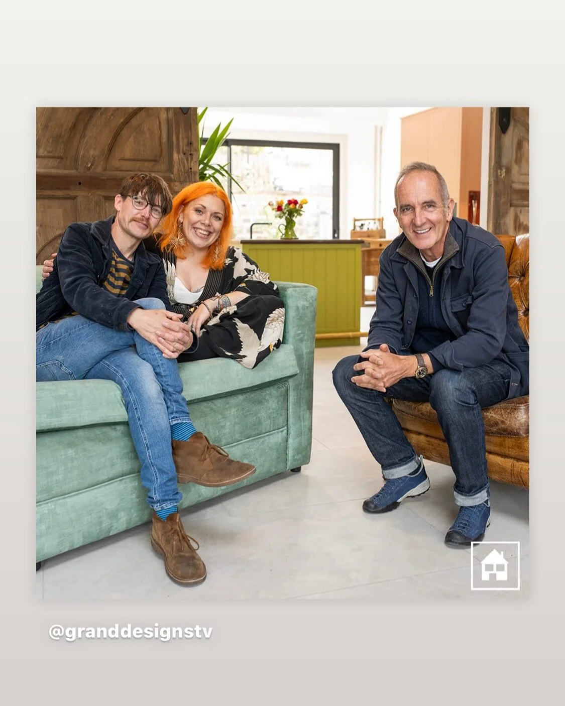 Grand Designs final filming for the 25th year anniversary programme. Shot of Kara, Jonny & Kevin Mc Cloud sitting on couches in a cozy indoor setting, smiling at the camera. Two are seated on a green couch, one on a brown leather couch.