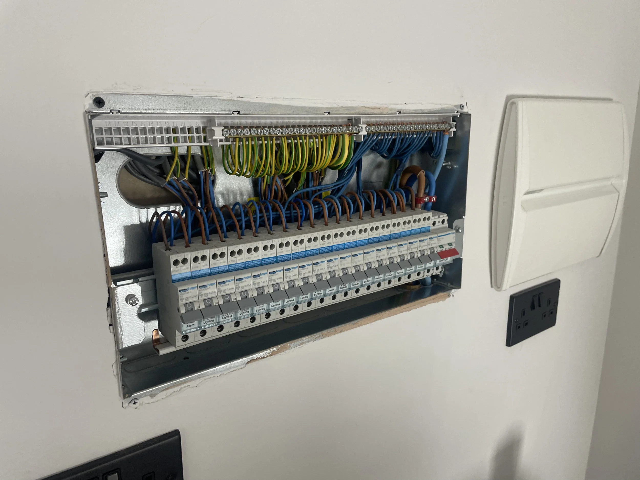 An electrical circuit breaker panel with multiple colored wires connected, mounted on a white wall.