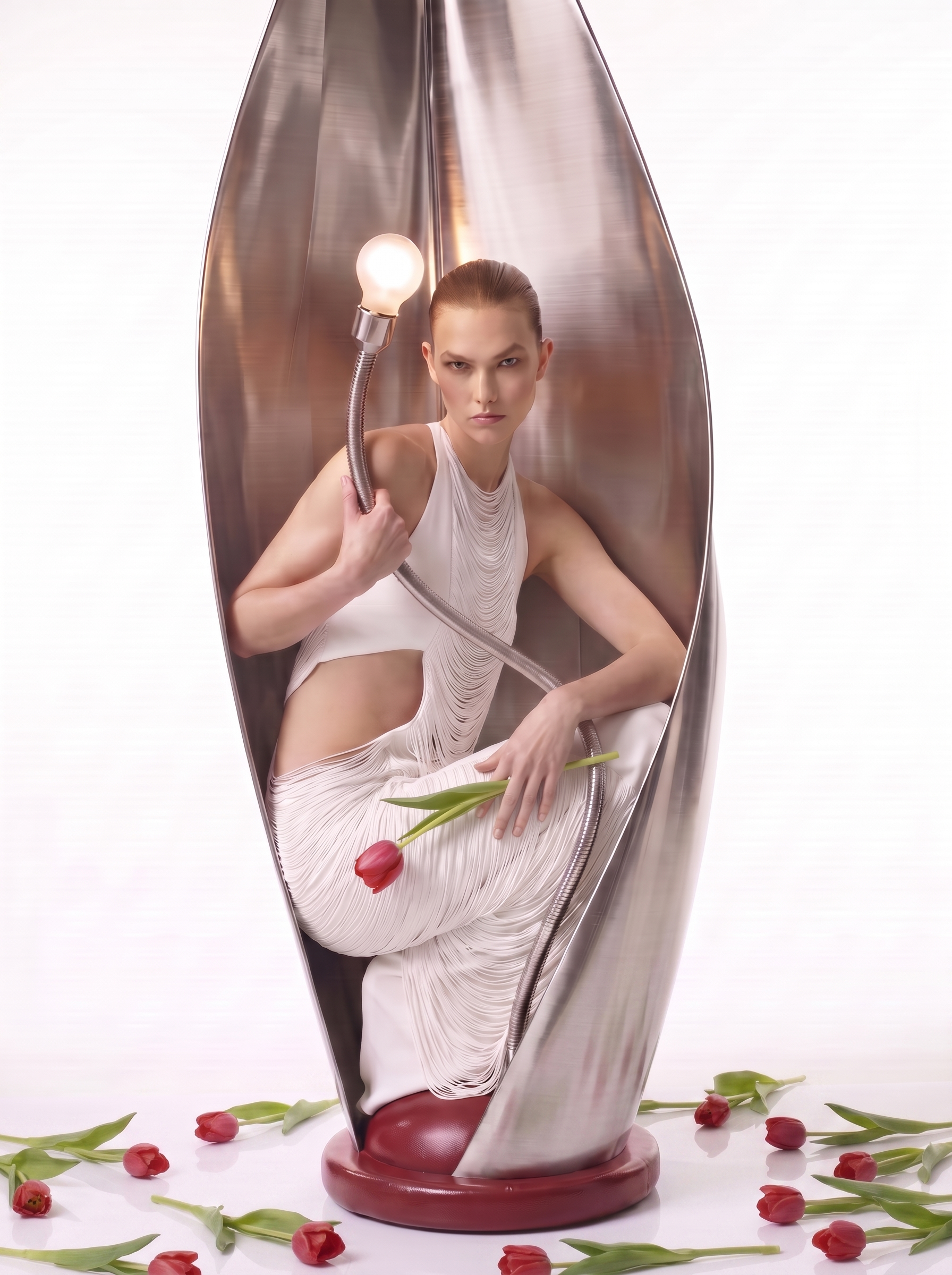 A reflective metallic sculpture of a woman in a dress holding a pink tulip, surrounded by scattered tulips on a white surface.