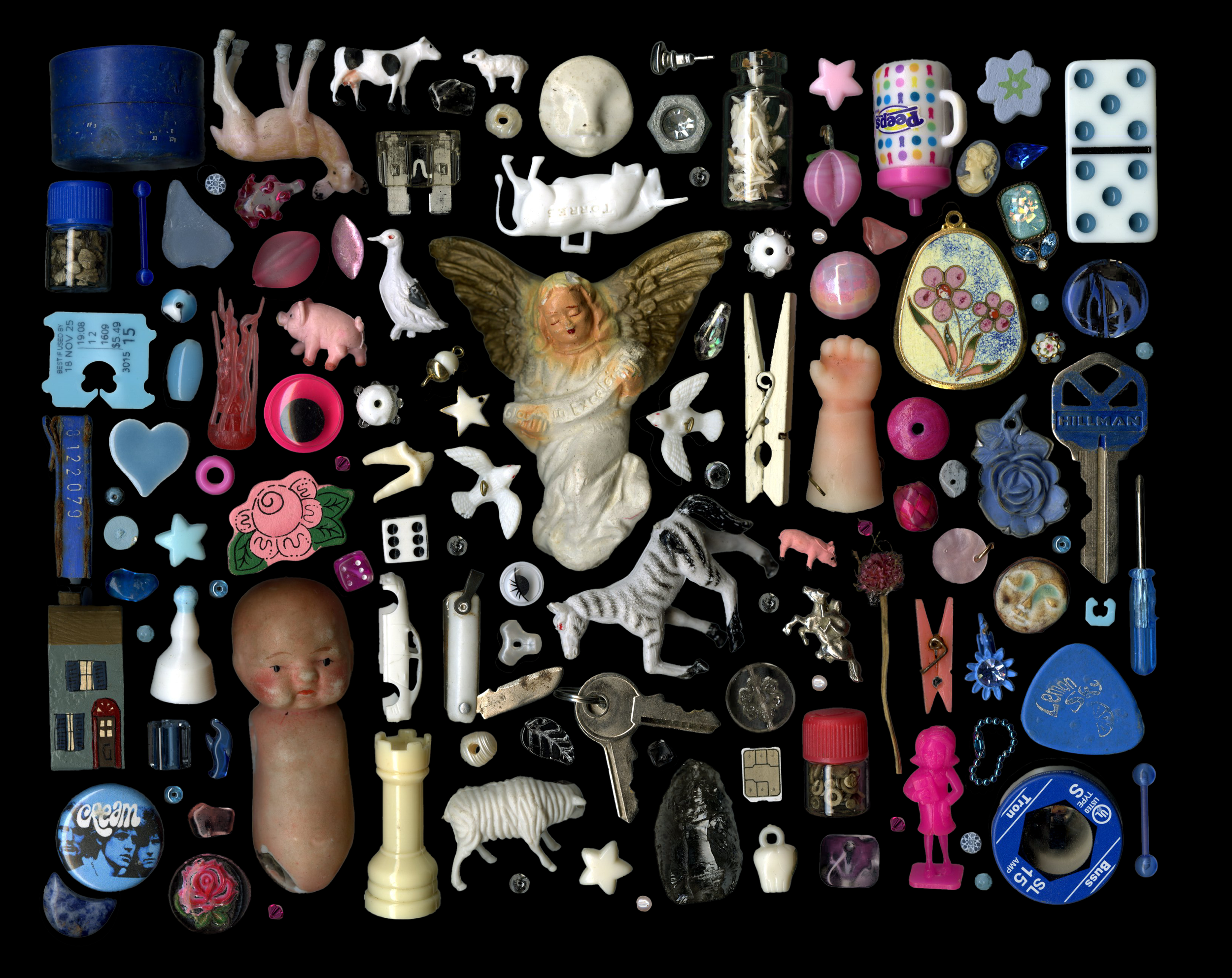 Collection of small toys, figurines, buttons, and assorted objects arranged on a black background, including a doll head, ceramic angel, dice, a tiny house, and various miniature figures.