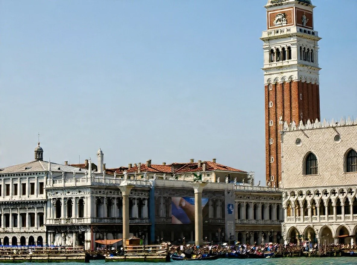 A view of a historic building in Venice with a tall bell tower, seen from across the water.