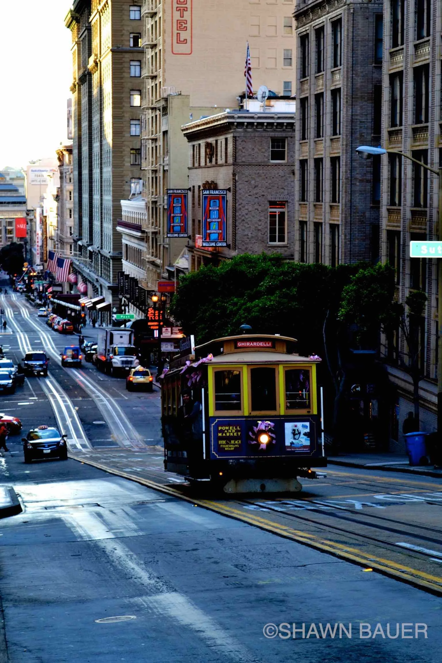 San Francisco cable car traveling down a steep city street with tall buildings on both sides, showcasing Union Square and advertisements, during daytime.