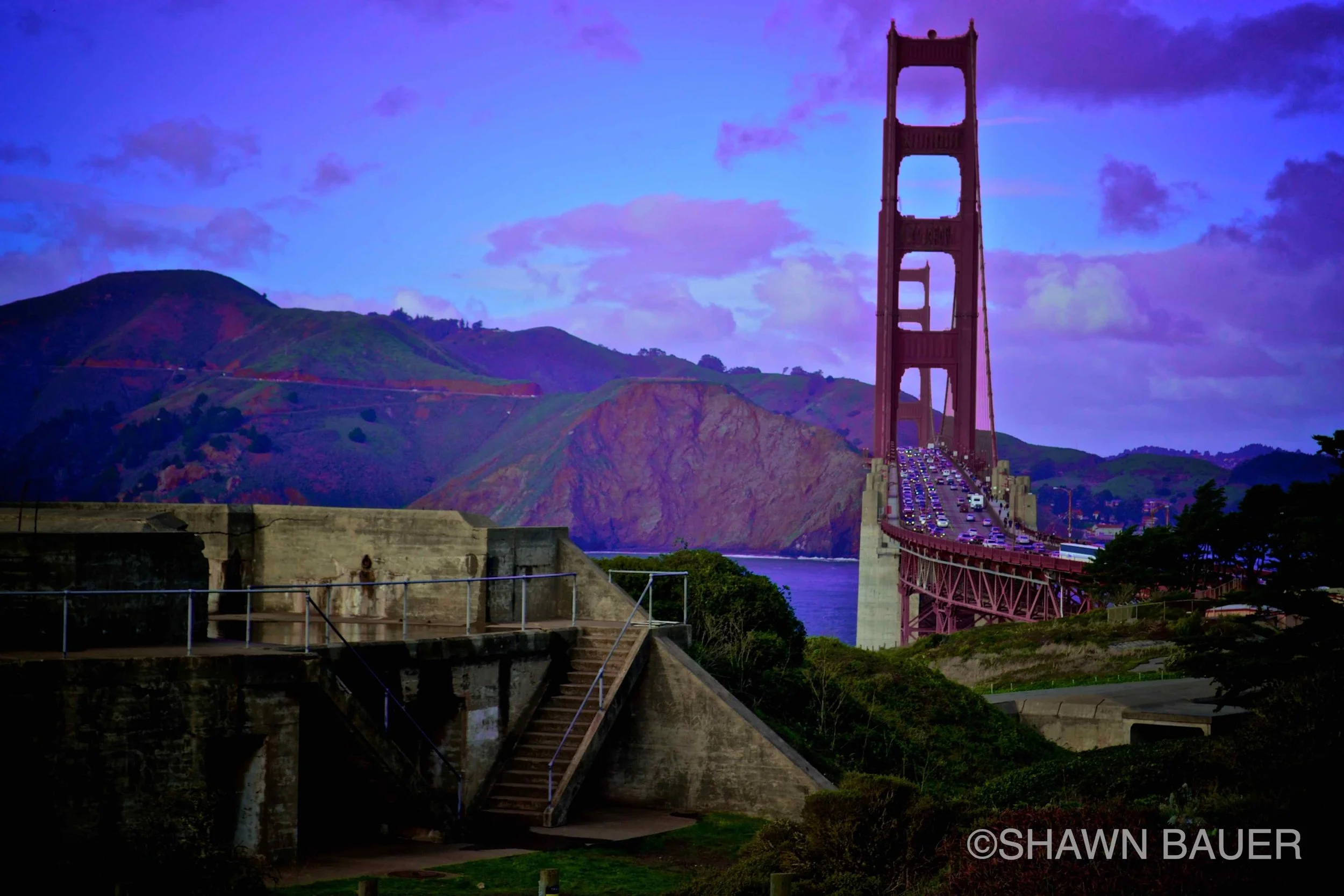 View of the Golden Gate Bridge during sunset with purple sky and mountains in the background.