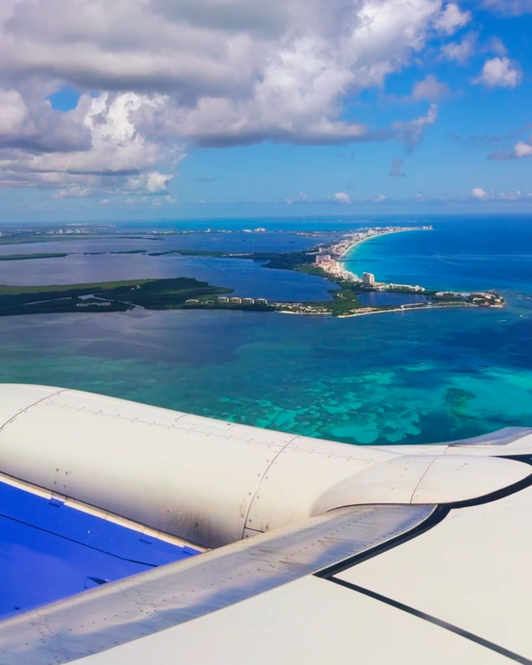 Airplane wing view over turquoise water and islands in the Caribbean