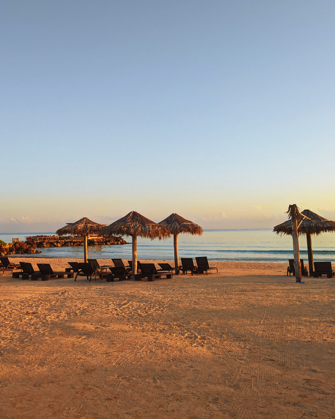 Thatched-roof beach loungers at sunset on a tropical shoreline