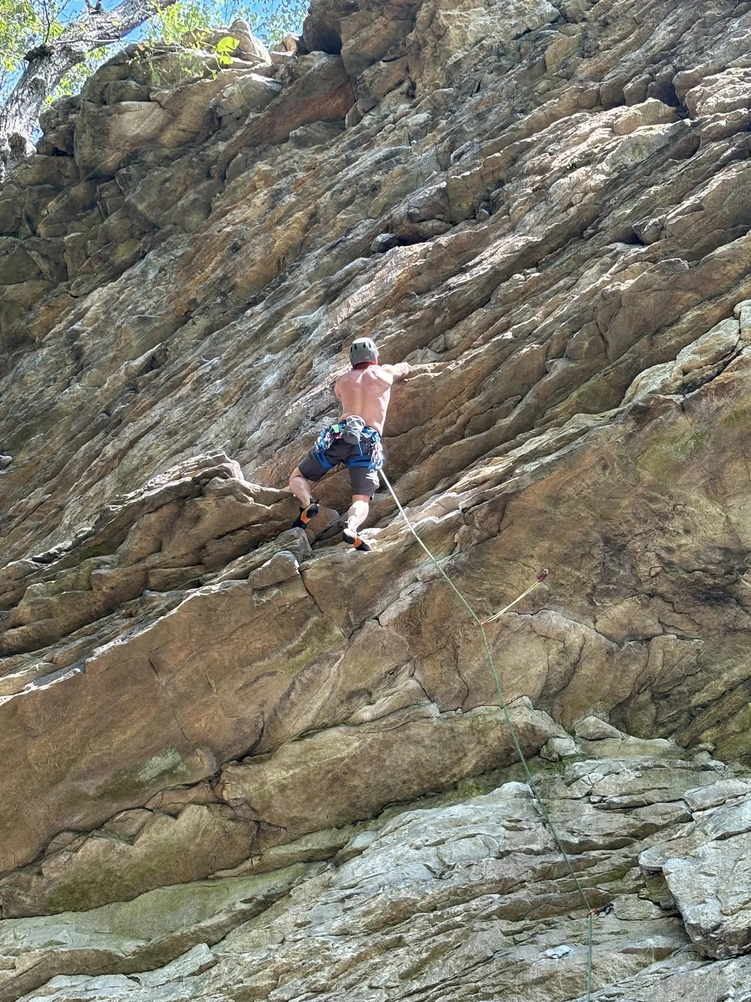 A person rock climbing on a steep, rocky outdoor cliff, wearing a helmet and climbing gear.