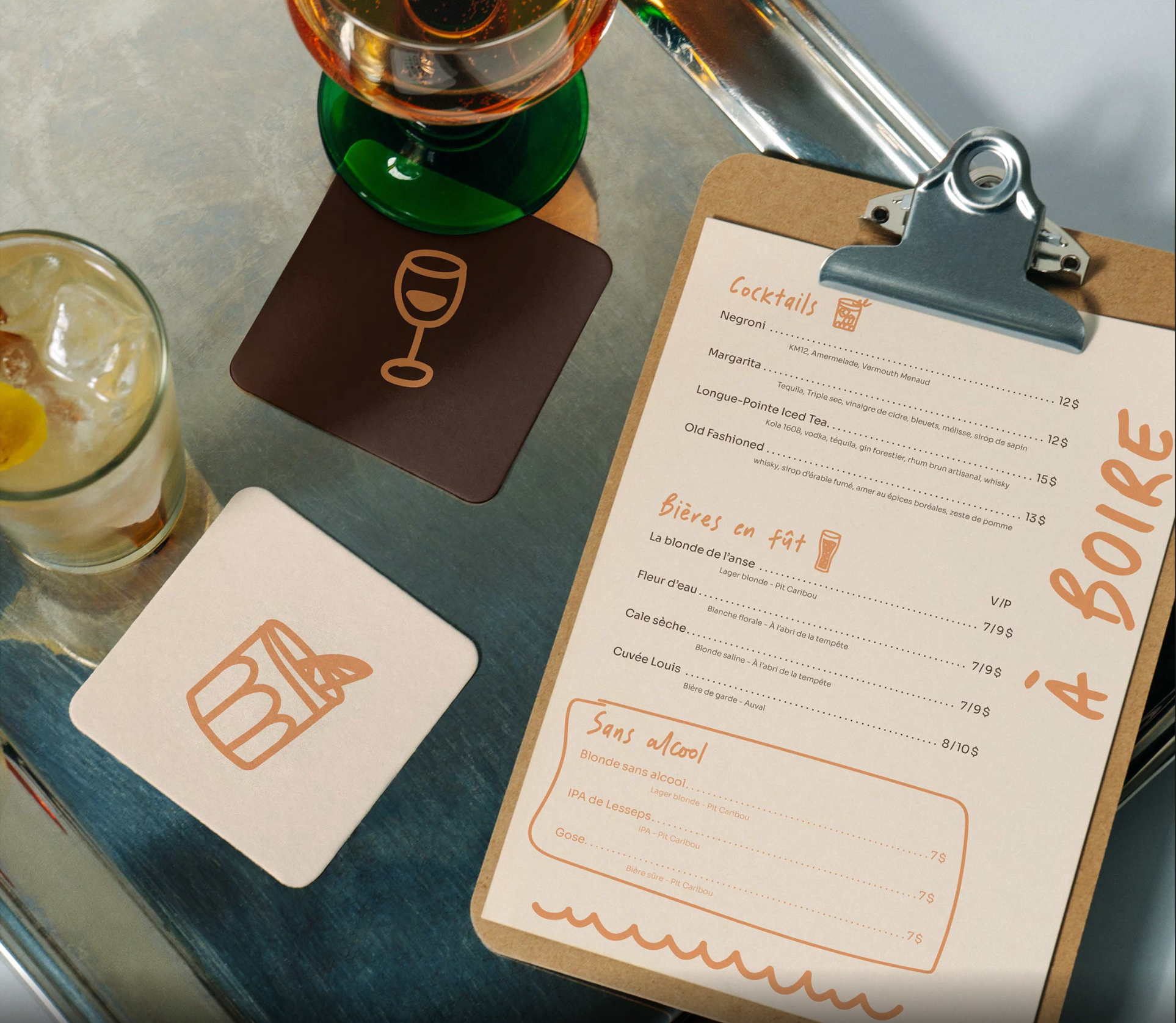 Une table avec une boisson dans un verre, un menu de cocktails, et un sous-verre vert, le tout sur une surface en métal.
