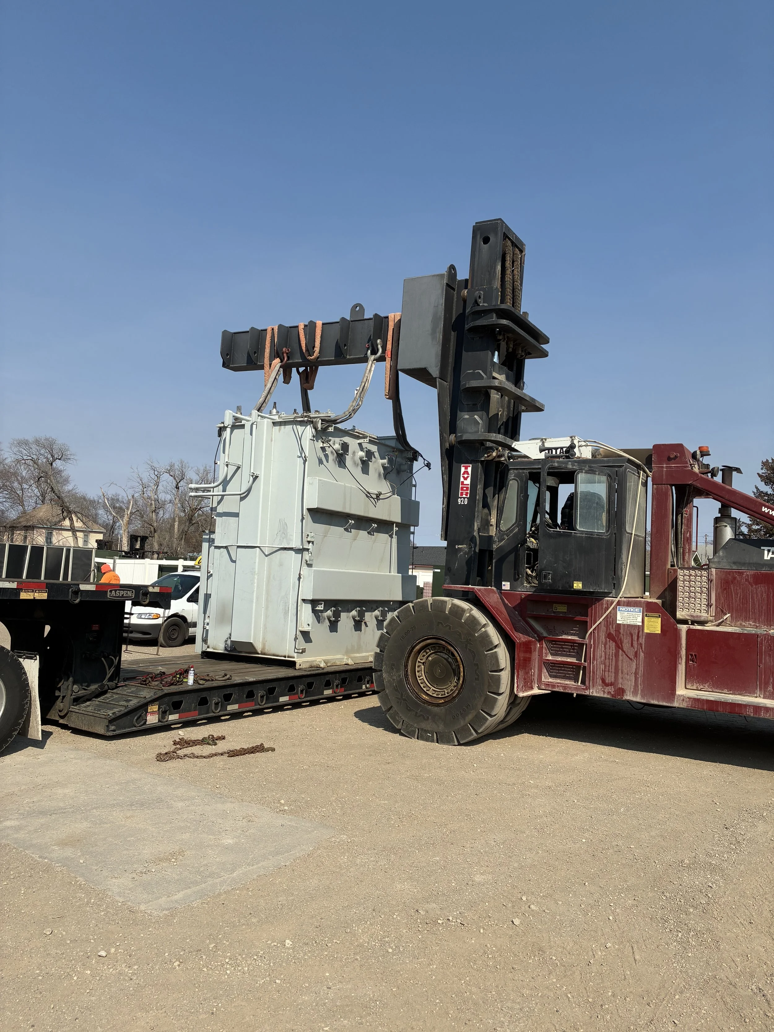 A large heavy-duty truck with a crane lifting equipment at a construction site under a clear blue sky.