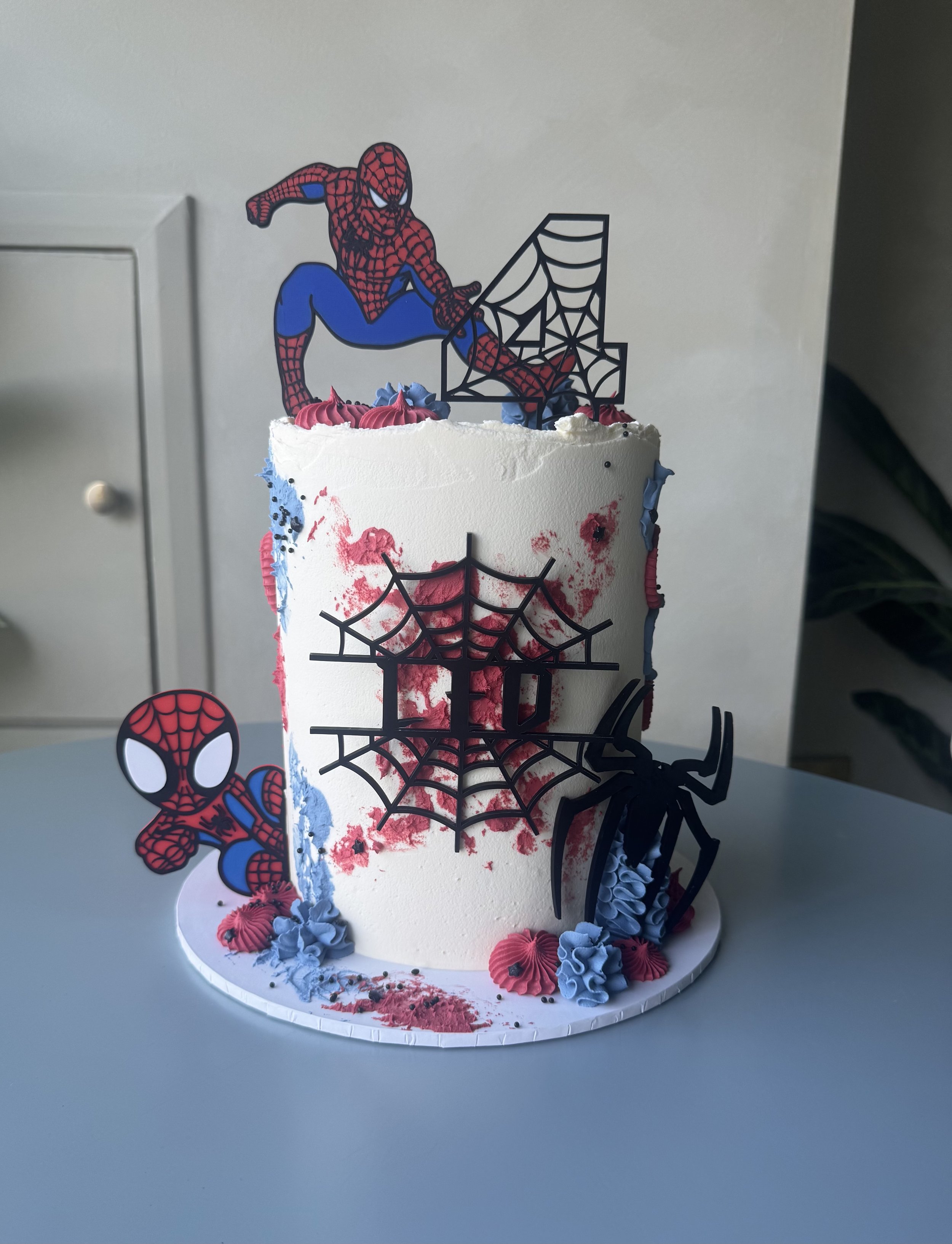 A Spider-Man themed birthday cake decorated with Spider-Man character cutouts, spider webs, and pink and blue frosting flowers.