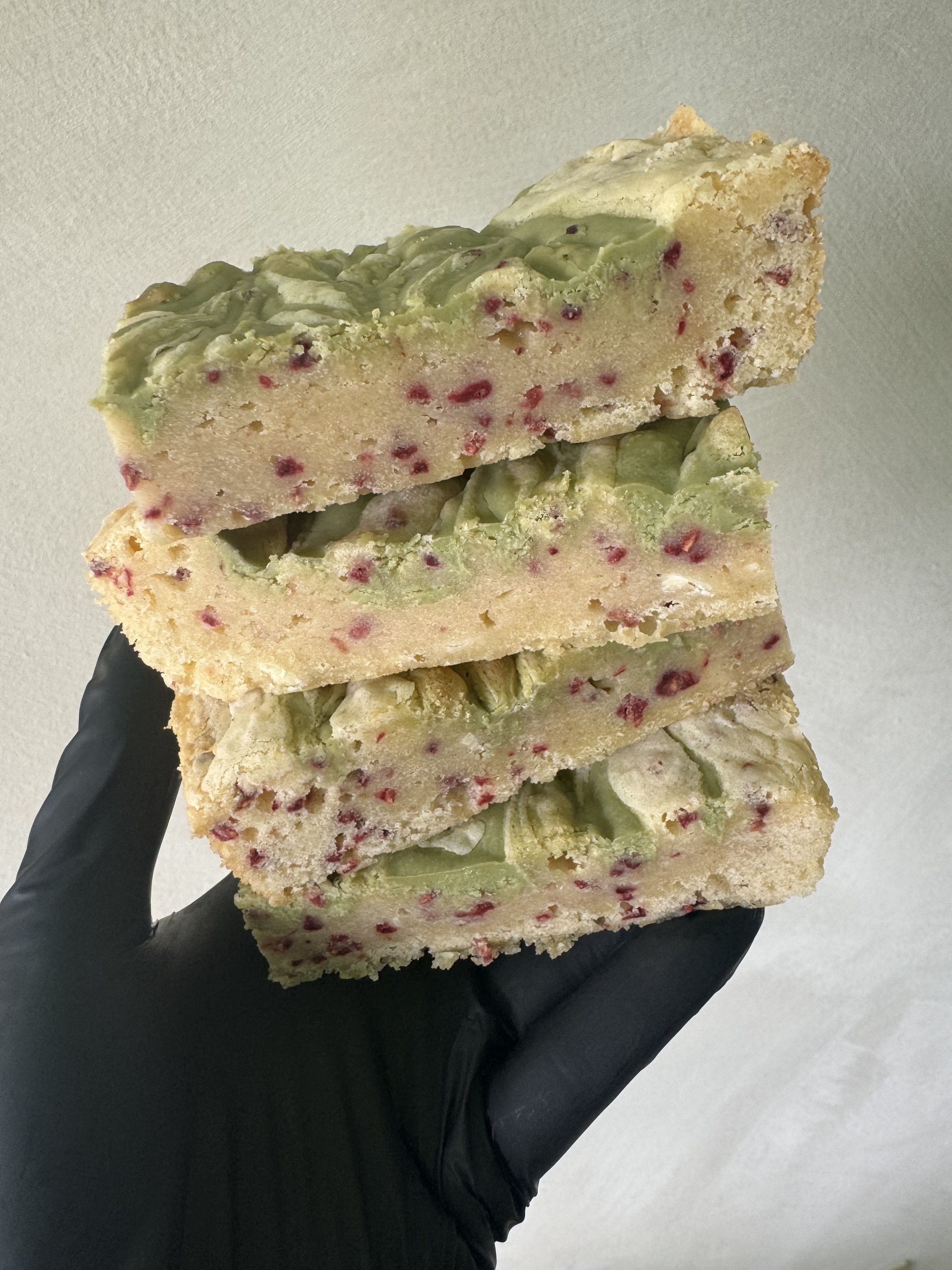 Stack of three rice crispy treats with green and red bits, held in a black glove.