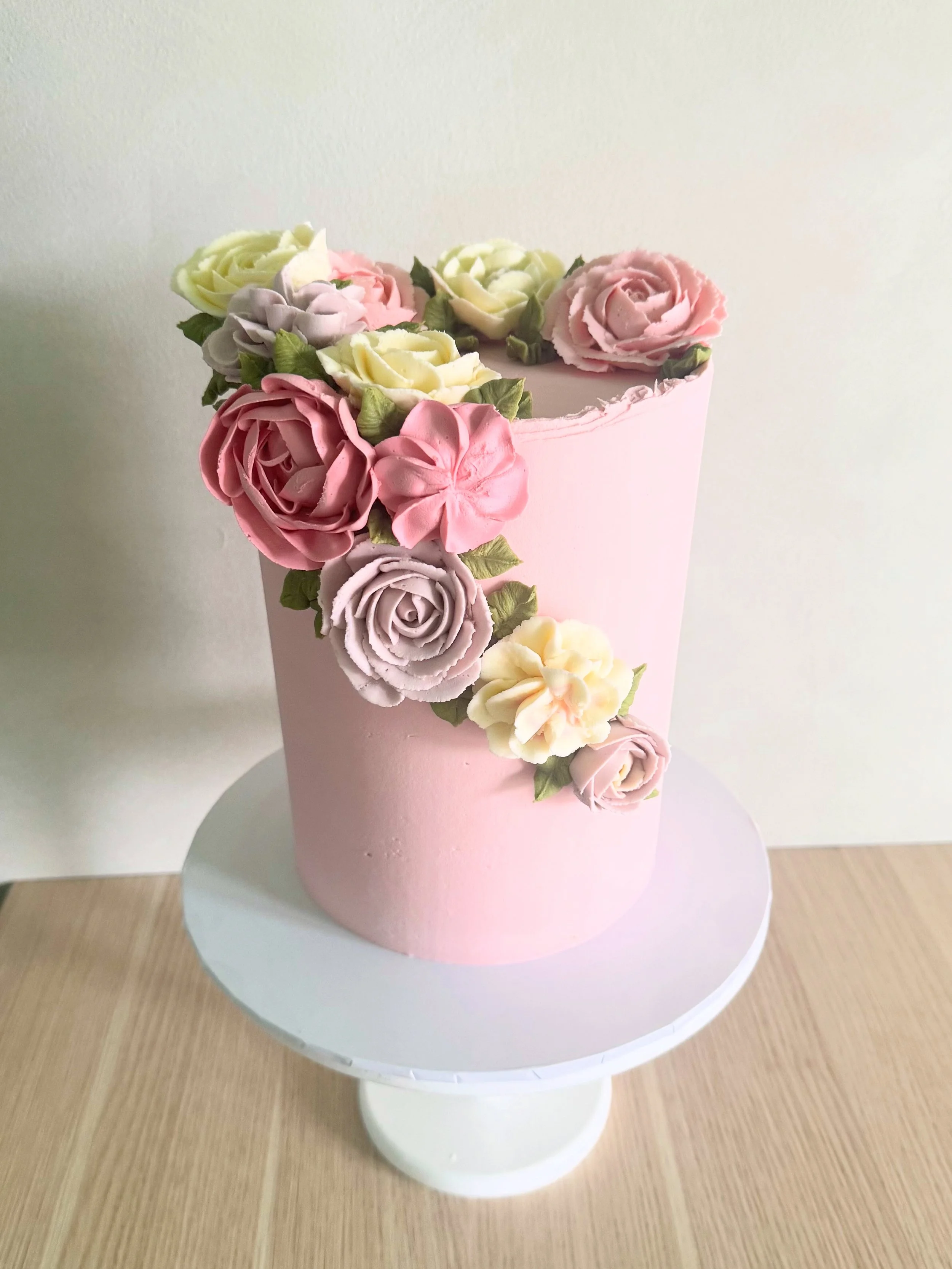 Pink cake decorated with buttercream roses in pastel colors placed on a cake stand.