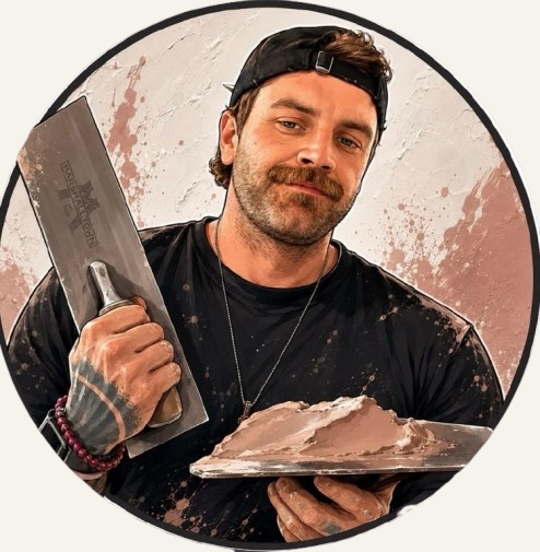 A man with a moustache and beard wearing a black cap backwards, black t-shirt, and bracelets on his wrist, holding a large knife in one hand and a metal tray with chocolate in the other, standing against a textured wall.