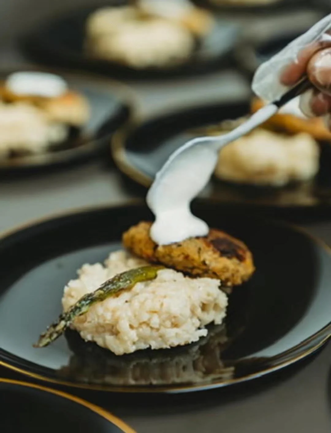 Plated risotto topped with a vegan crab cake, asparagus spear and spooned dollop of roasted garlic aioli.