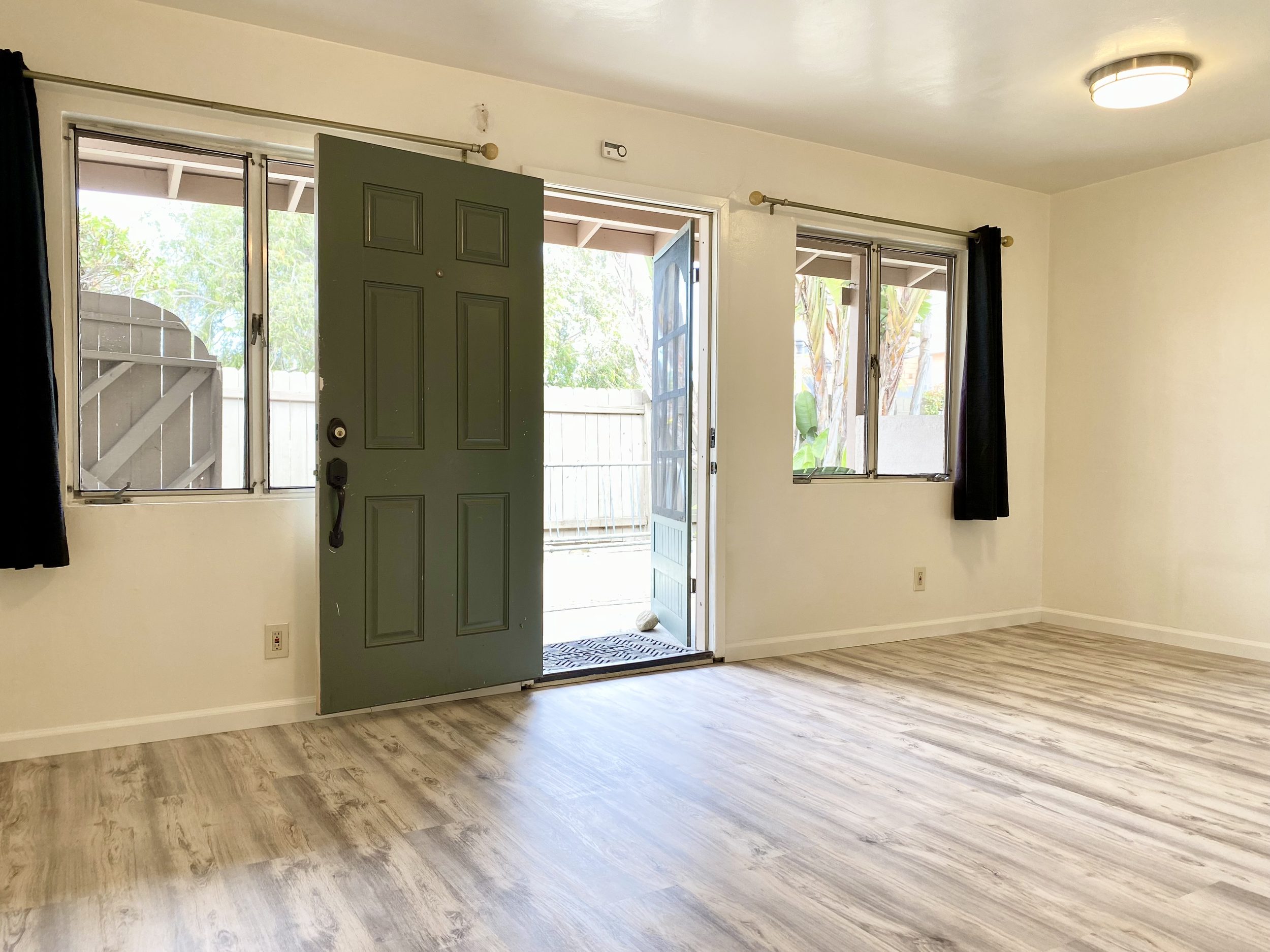 Open front door with two windows on either side, revealing a small outside area with trees.