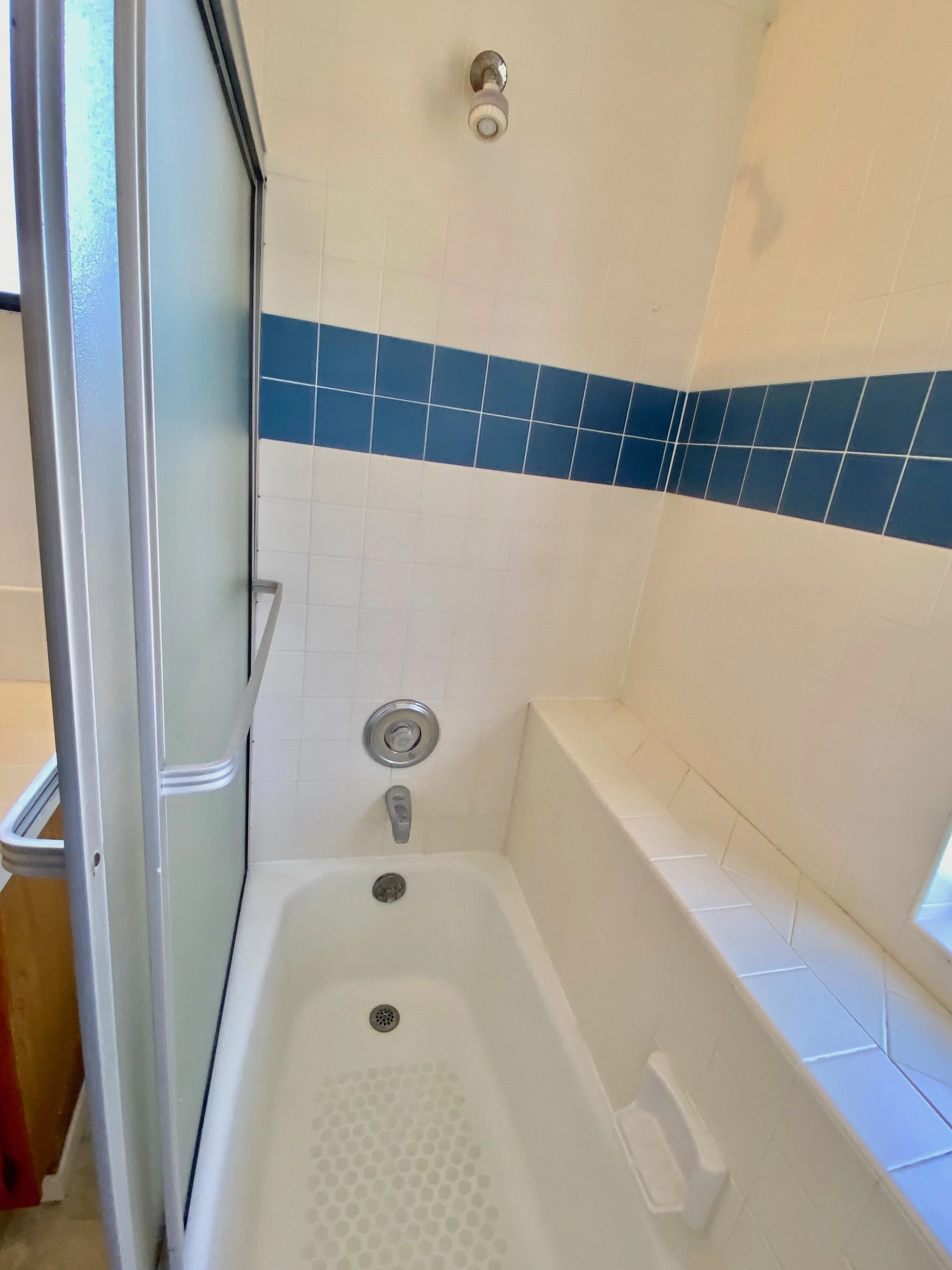 Bathroom shower with a frosted glass sliding door, white tiles with a blue horizontal stripe, a shower head, and a built-in bench.