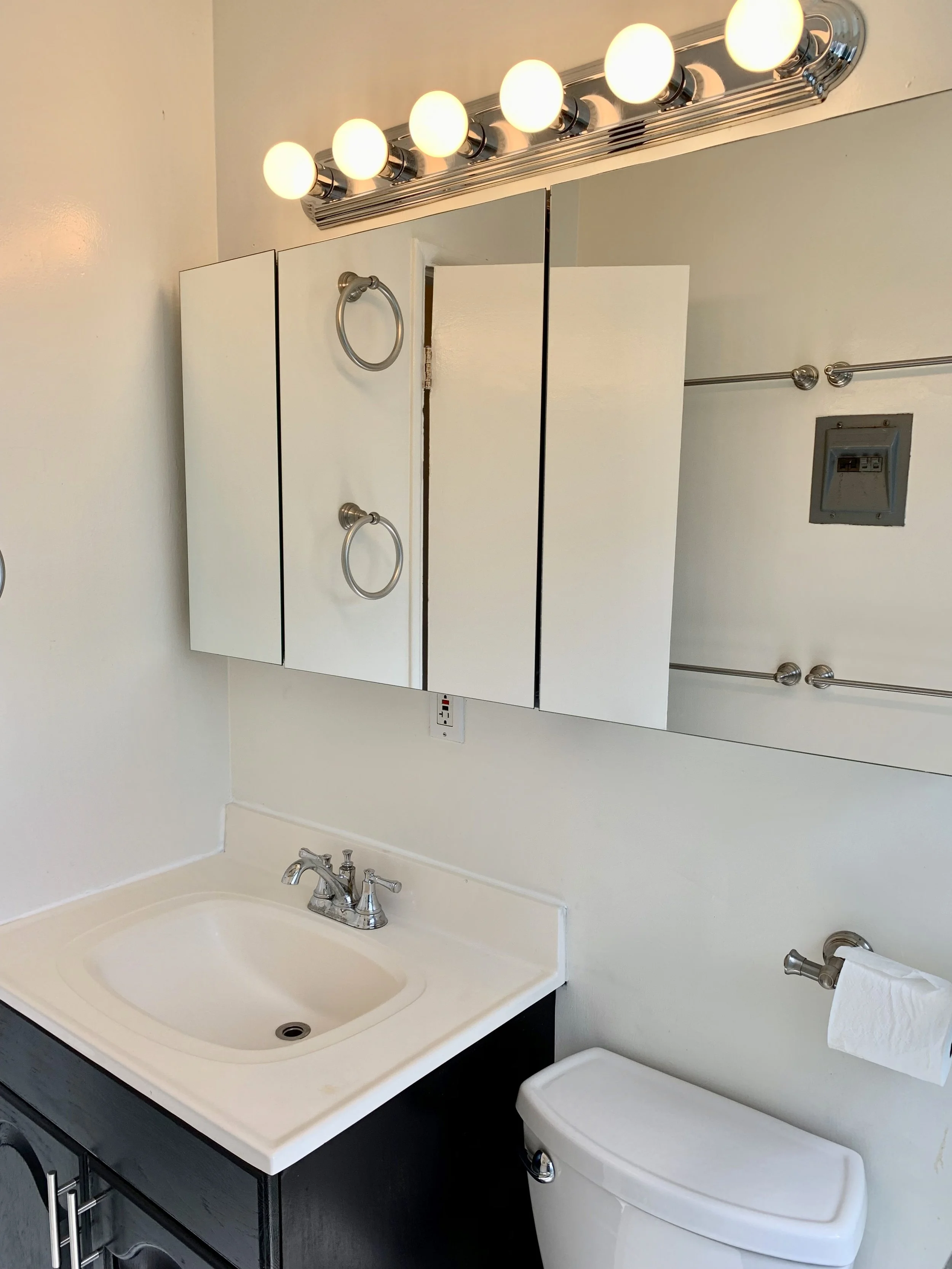Bathroom with a sink, vanity mirror, lights, towels, and a toilet.