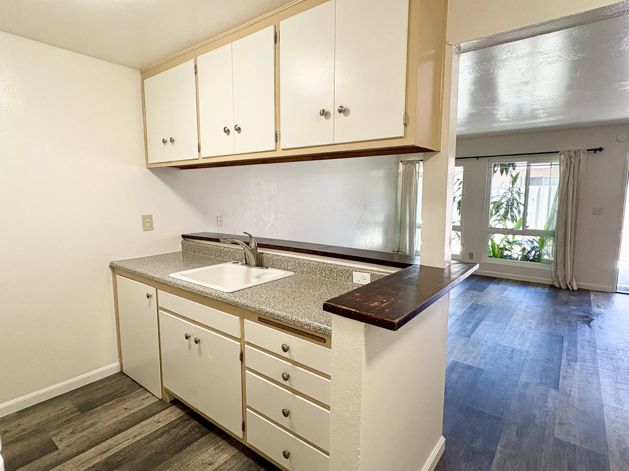 Kitchen with white cabinets, a granite countertop, a sink, and a view into a living area with large windows and curtains.