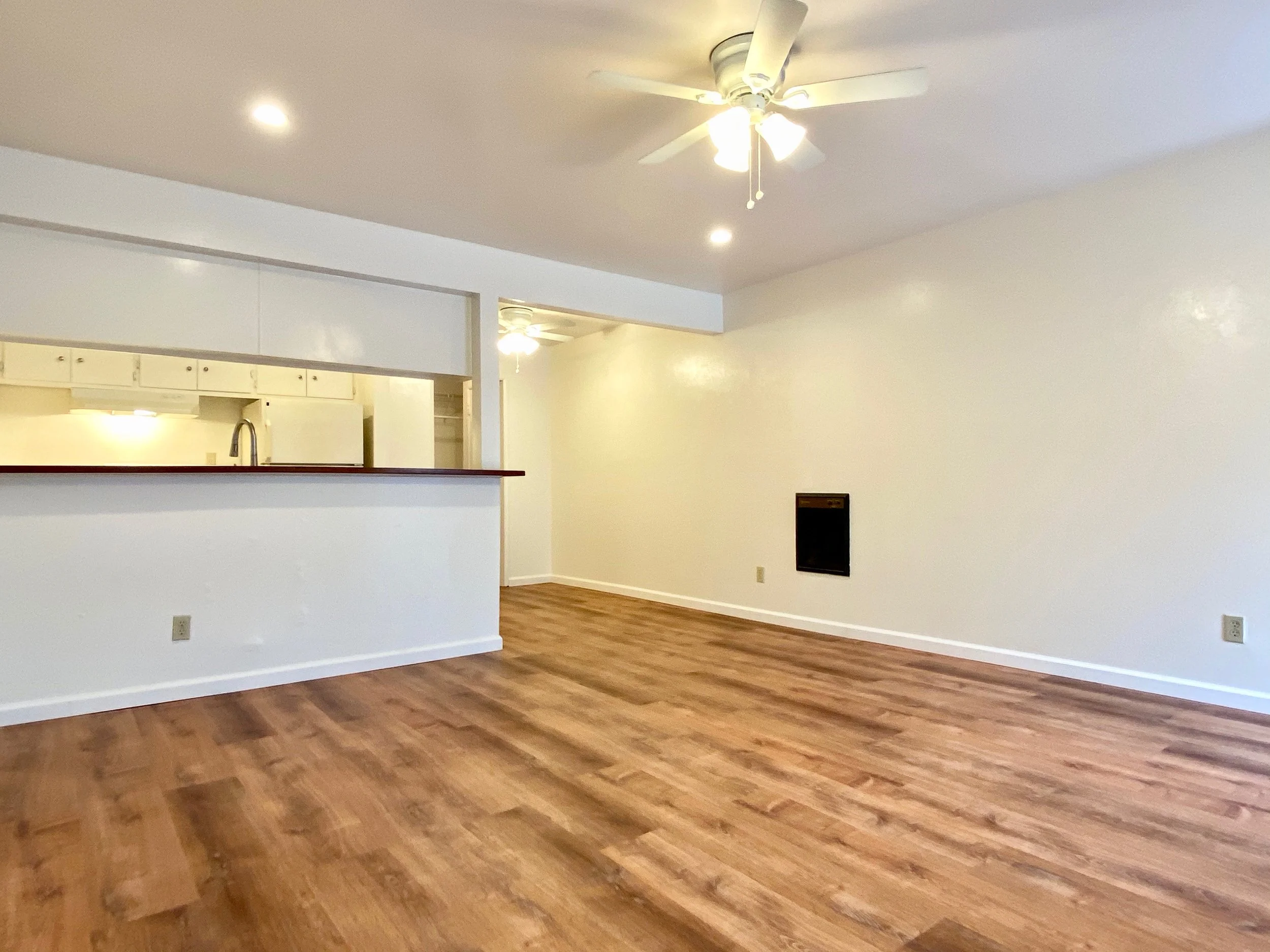 Empty living room with wood flooring, white walls, a ceiling fan with light, and recessed ceiling lights.