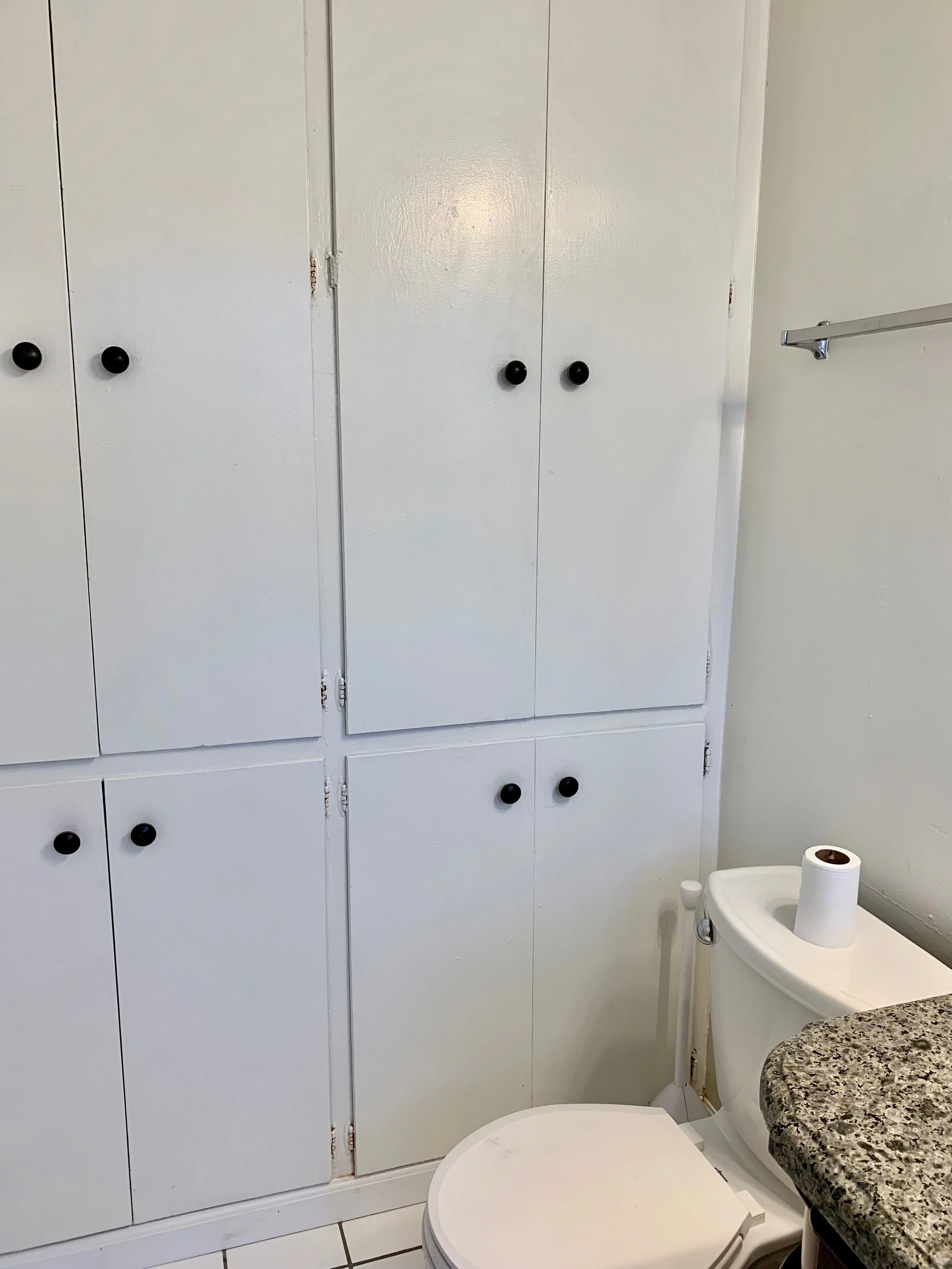 Bathroom with white cabinets, a toilet with a toilet paper roll on top, and a granite countertop.