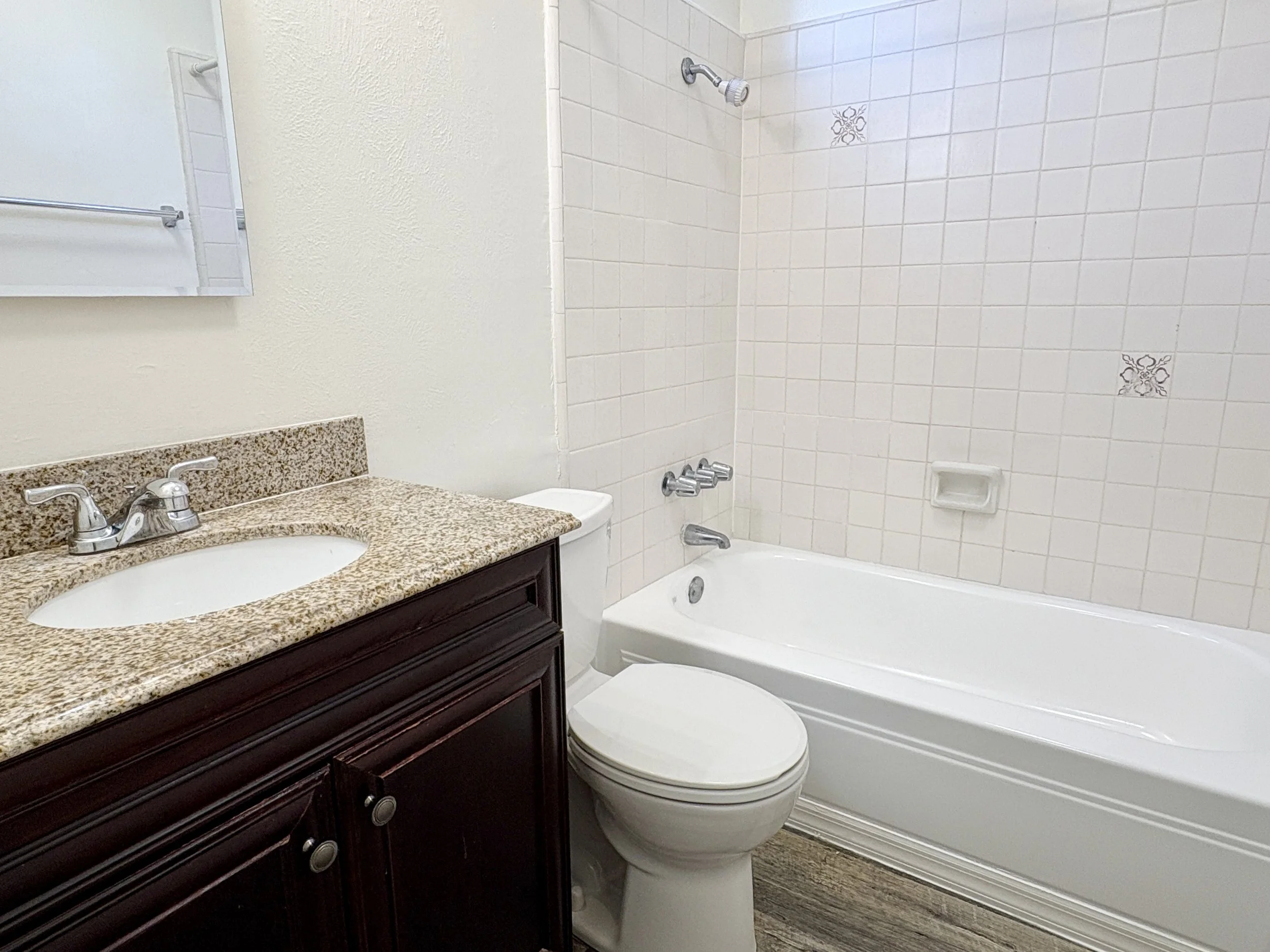 Bathroom with a granite countertop vanity, toilet, bathtub, and tiled walls.