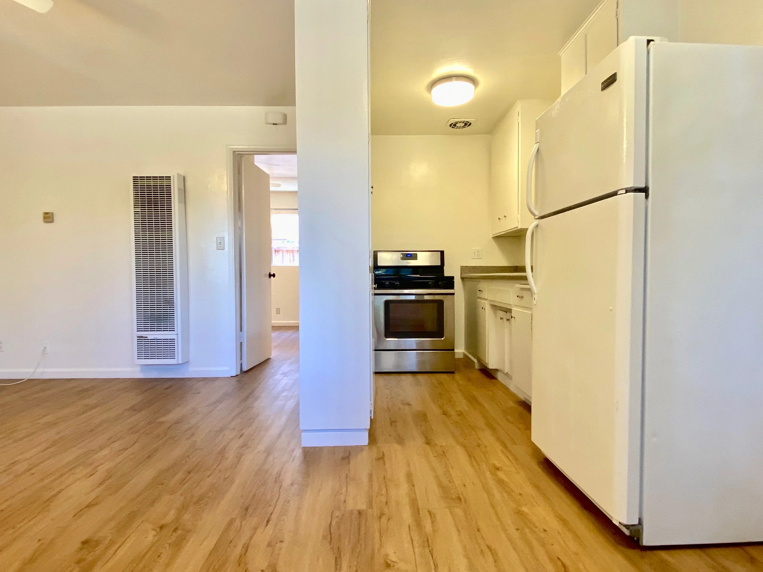 A kitchen with white cabinets, a white refrigerator, a black stove, wooden flooring, and a ceiling light