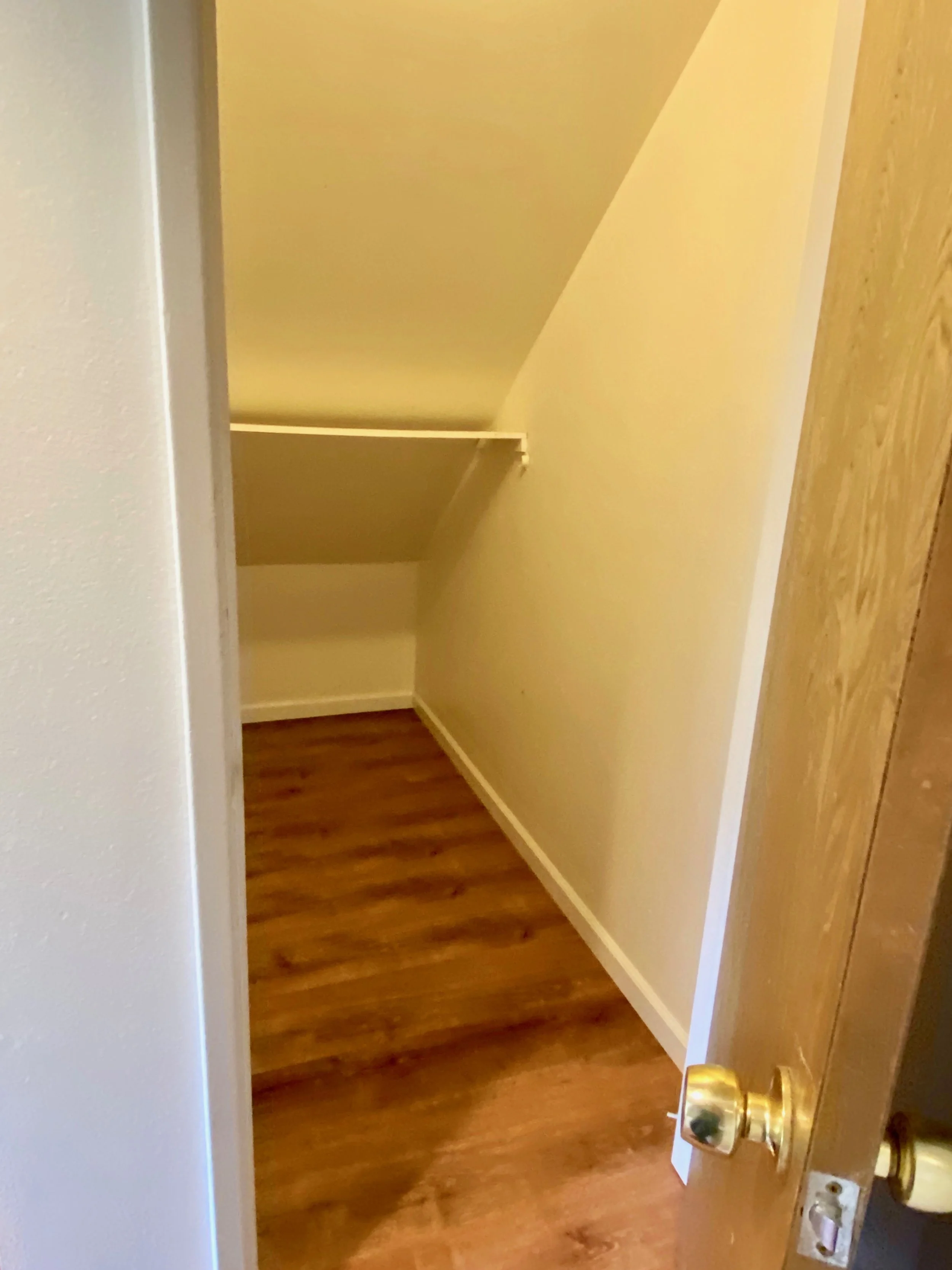 View of a small empty room with light yellow walls and wooden floor, seen through a partially open door with a brass doorknob.