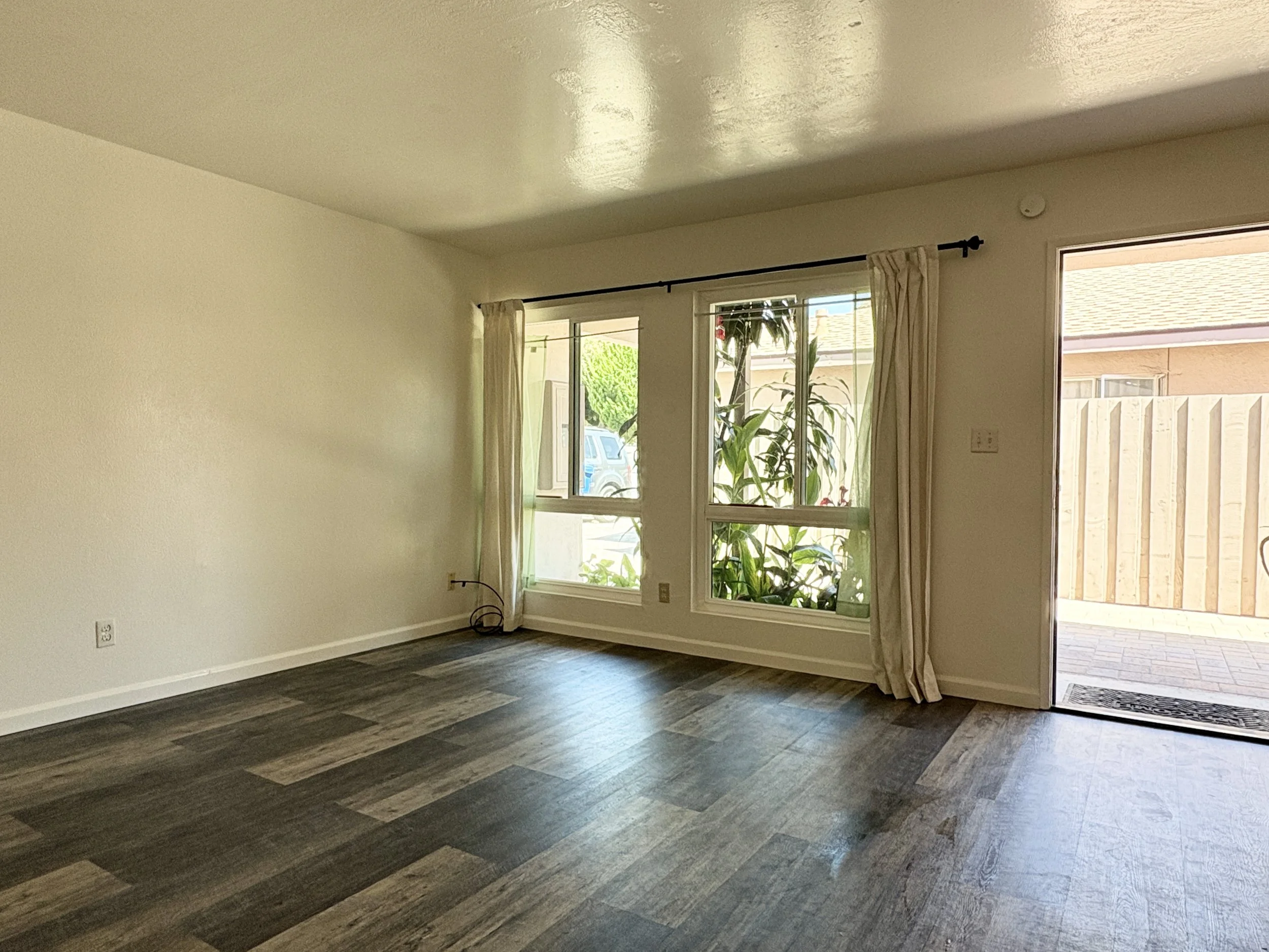 Empty room with large windows, curtains, and wood flooring.
