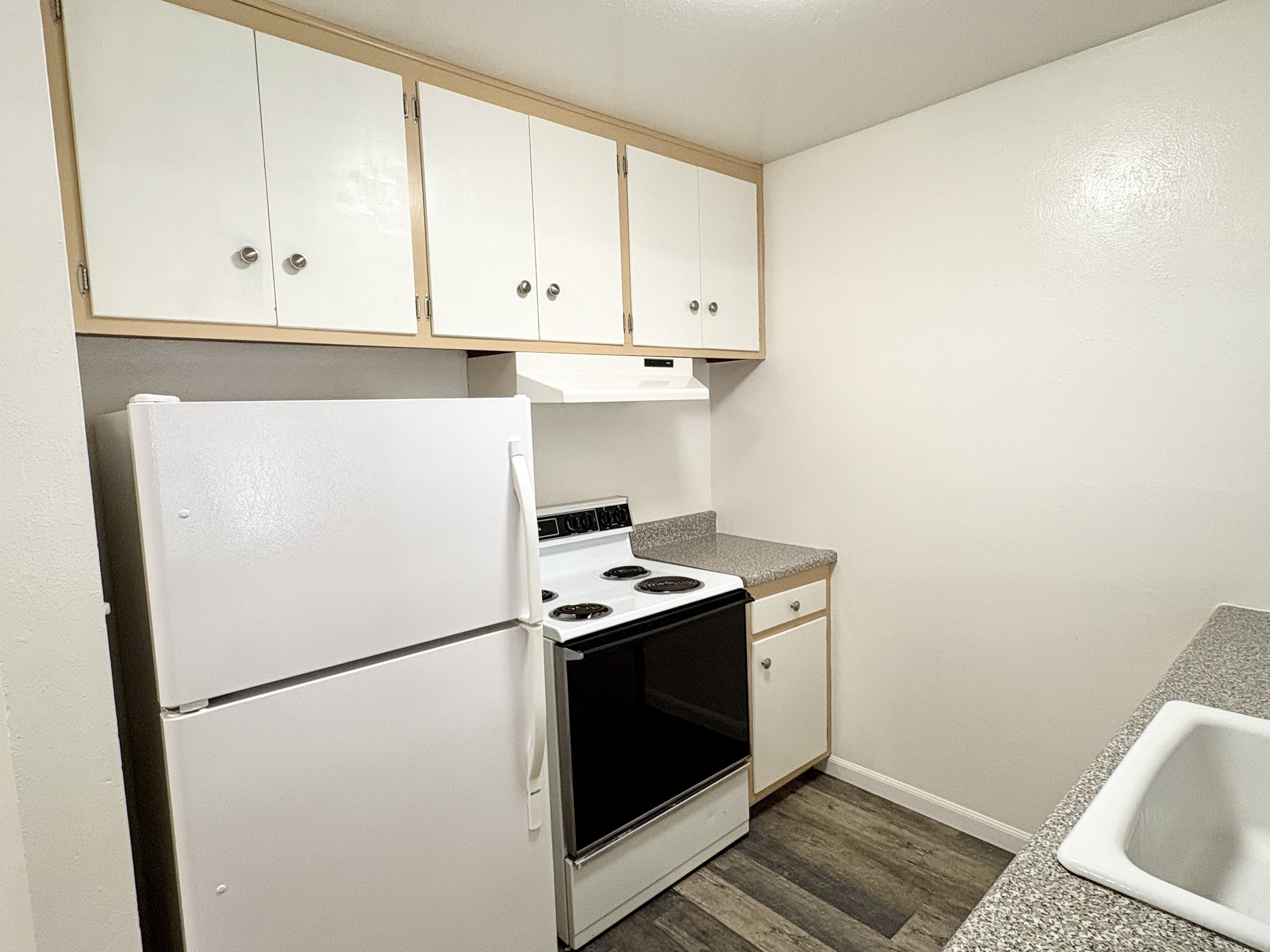 A small kitchen area with white cabinets, a white refrigerator, an electric stove, granite countertops, and a white sink with a faucet.