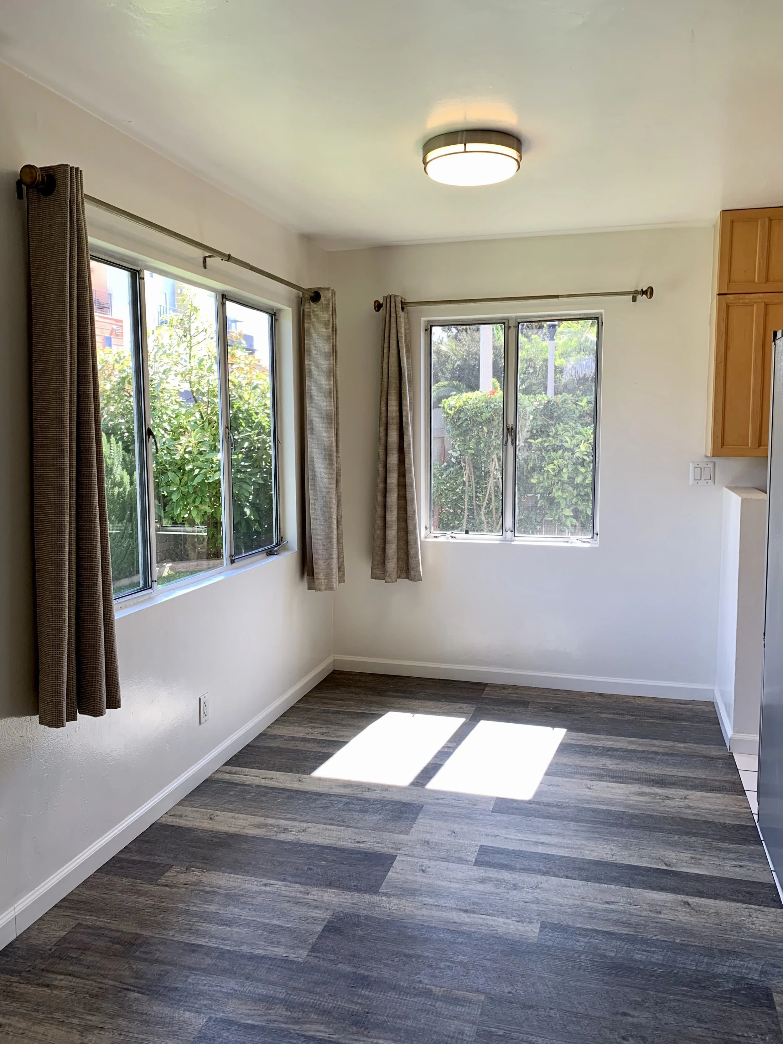 Empty room with wood-style flooring, two windows with beige curtains, and a ceiling light fixture.