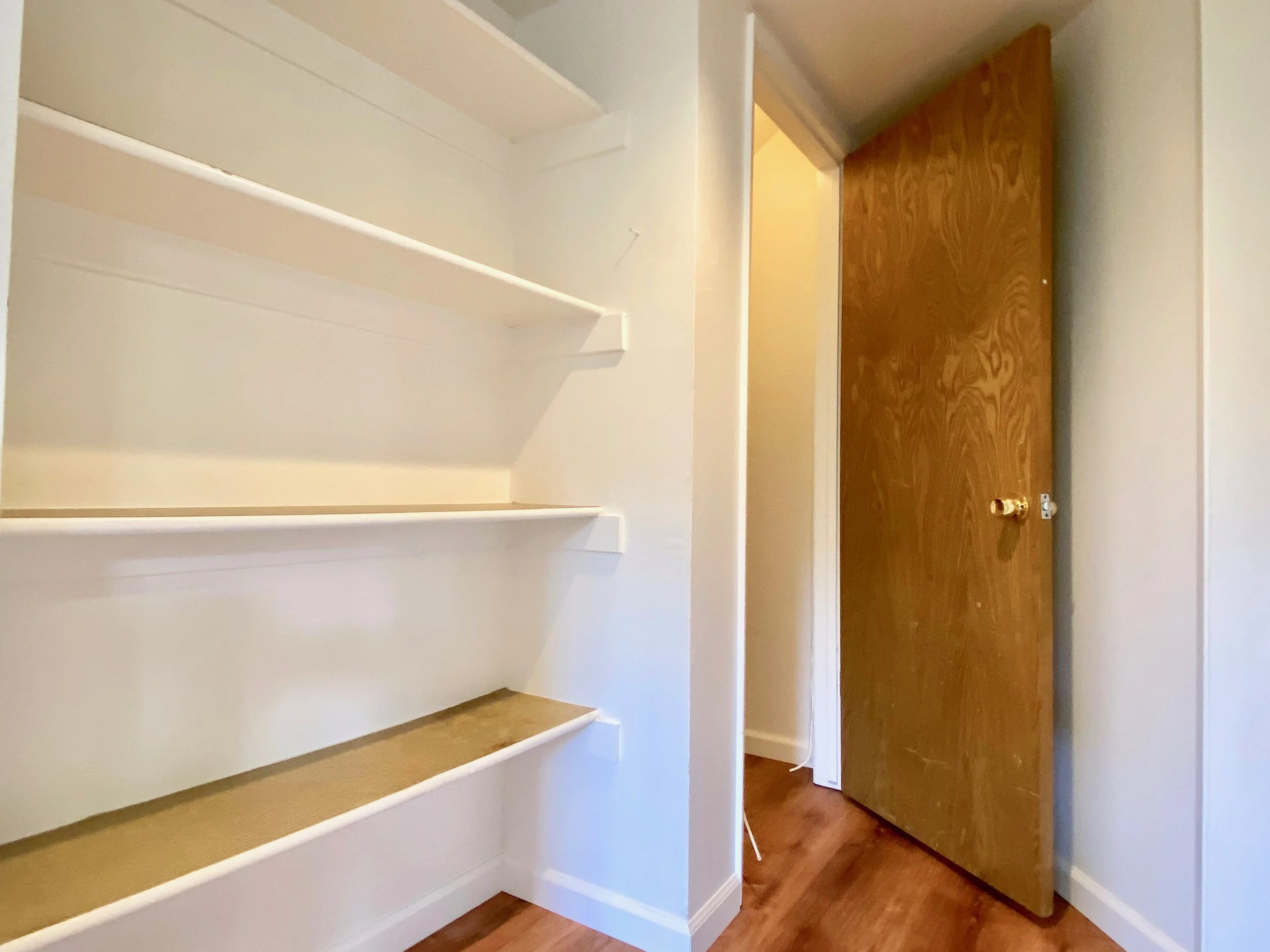 Empty white built-in shelves in a hallway leading to a brown wooden door.