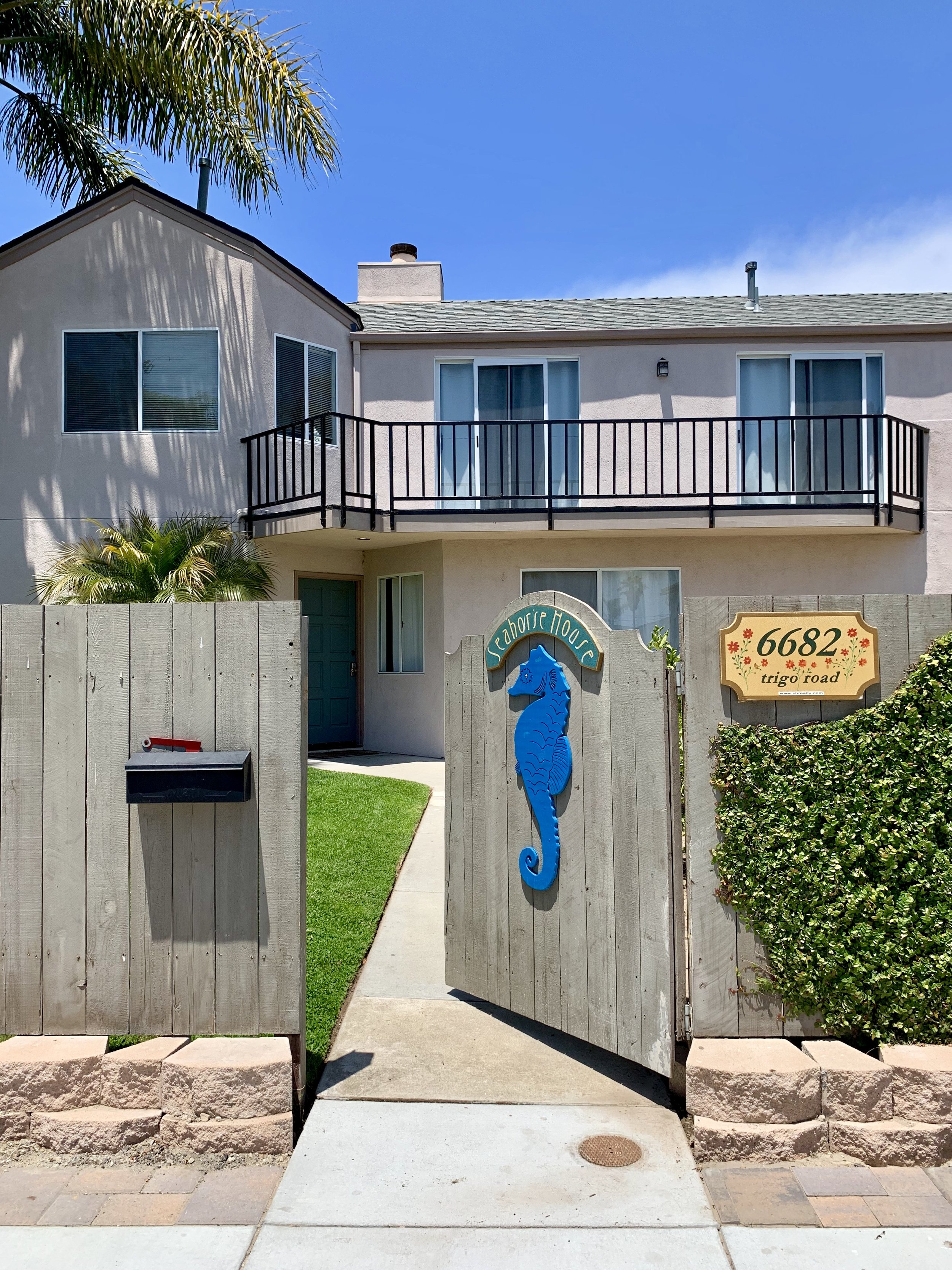 photo of the exterior of a 2-story house. There's an open gate in front with a Seahorse on it, and a sign that says "seahorse house".