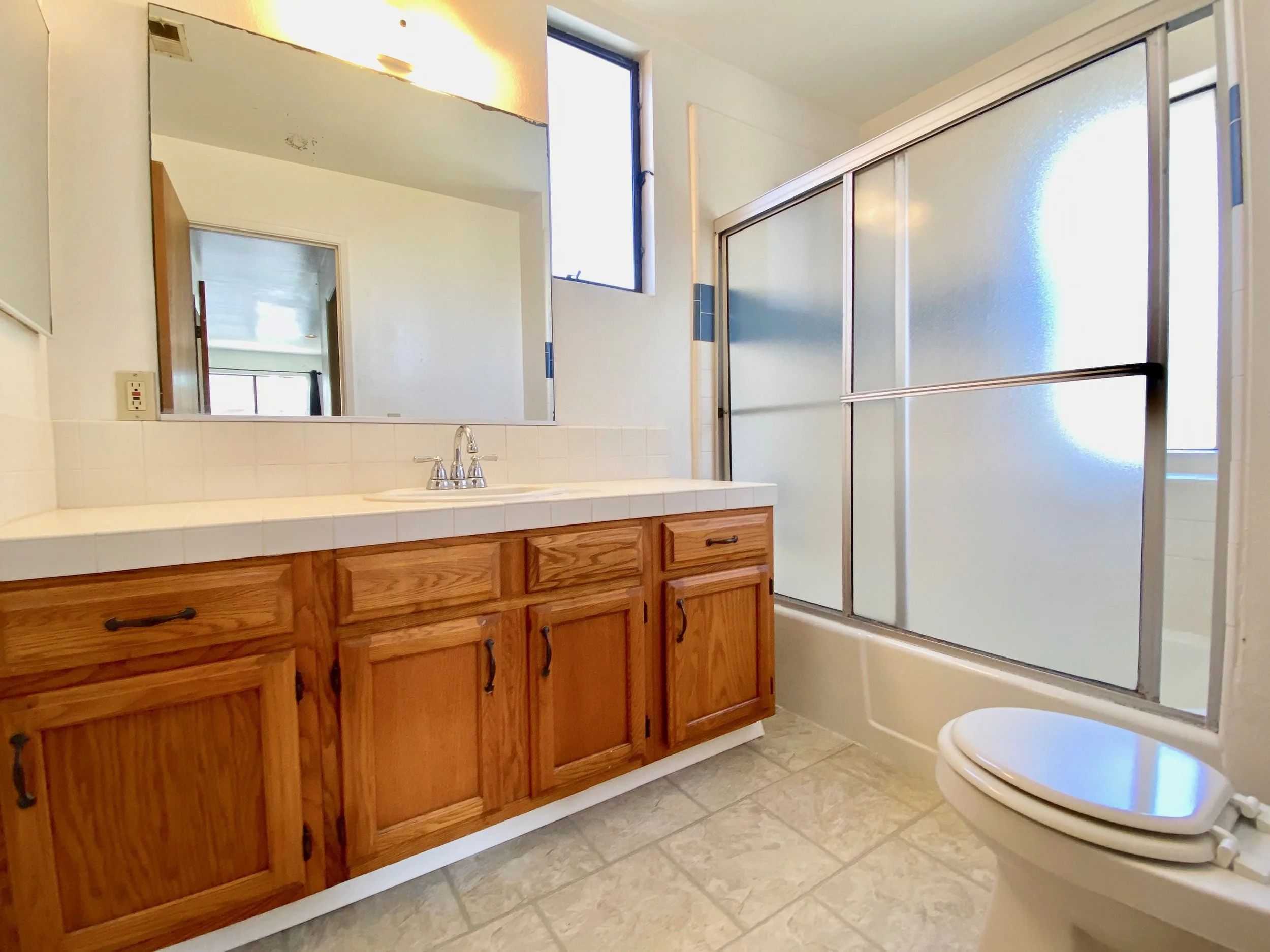Bathroom with wooden vanity, large mirror, frosted glass shower doors, and a toilet.