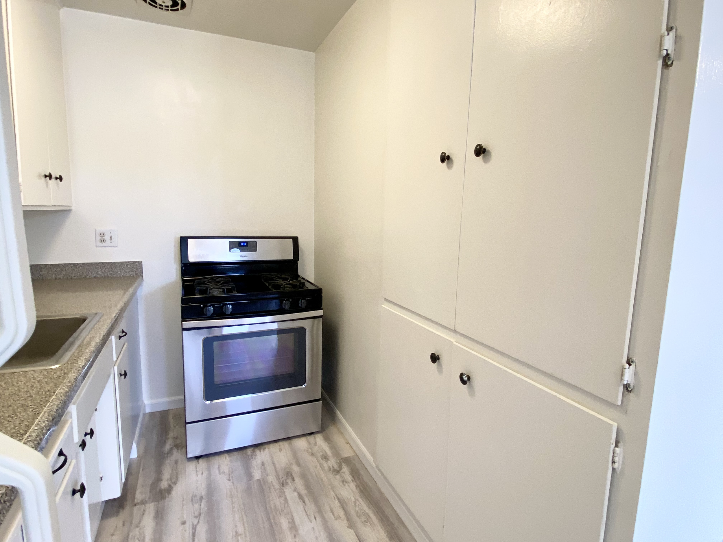 A small kitchen corner featuring white cabinets, a gray speckled countertop, a stainless steel stove, and wood-like flooring.