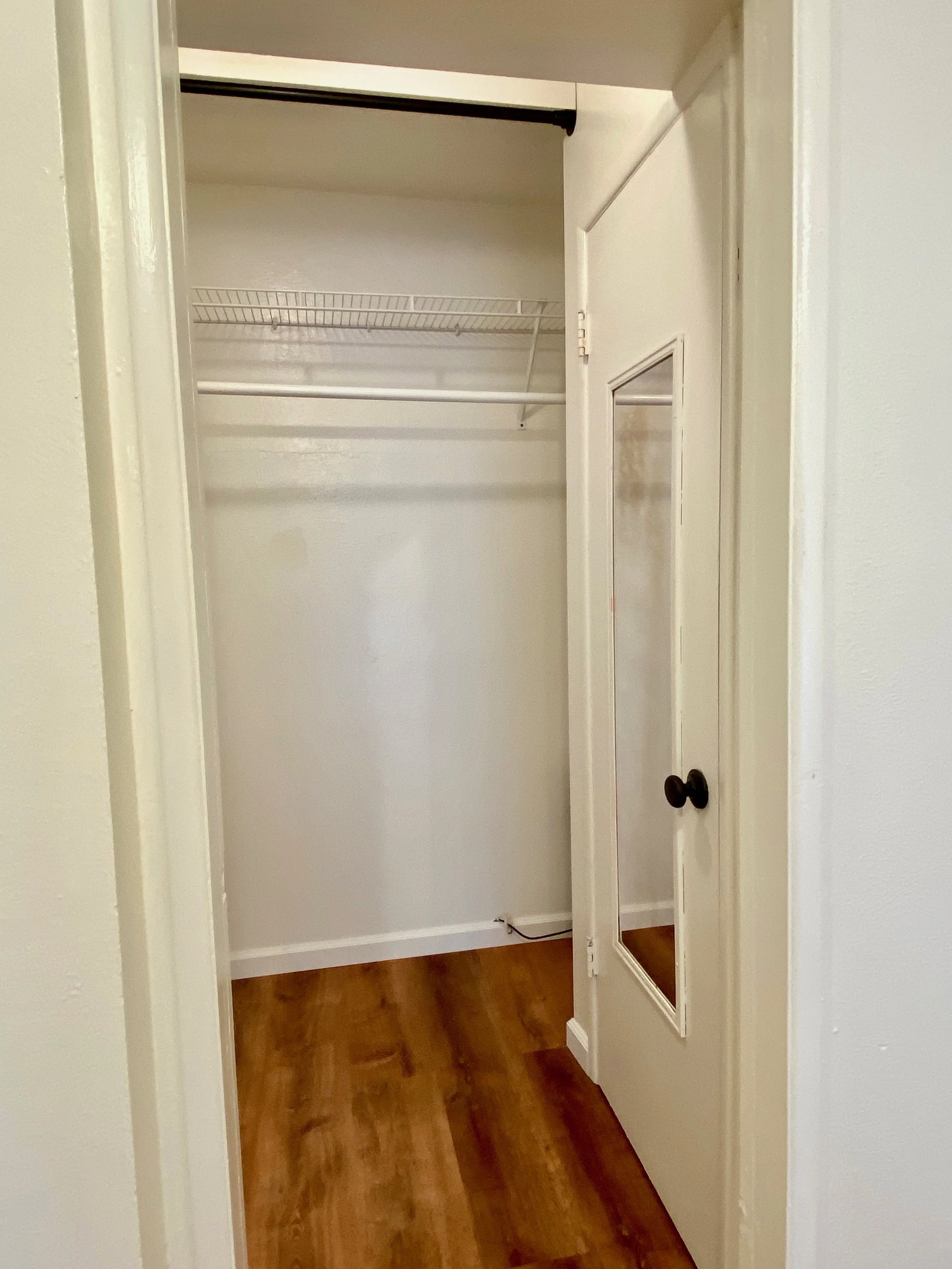 Empty closet with wire shelf, a sliding door with mirror, and hardwood floor.